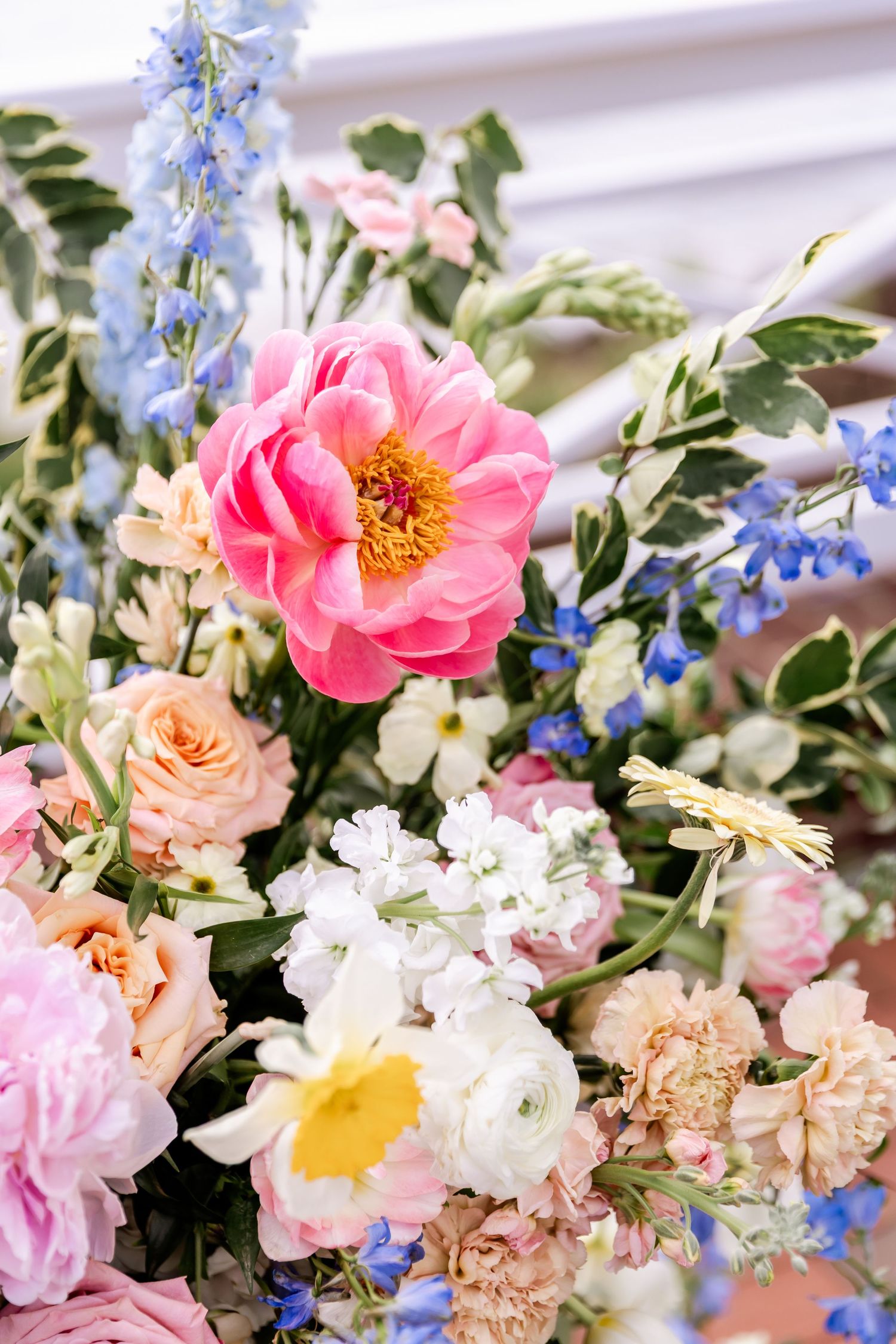 Colorful spring wedding bouquet with pink peonies, blue delphiniums, and white flowers in natural light.