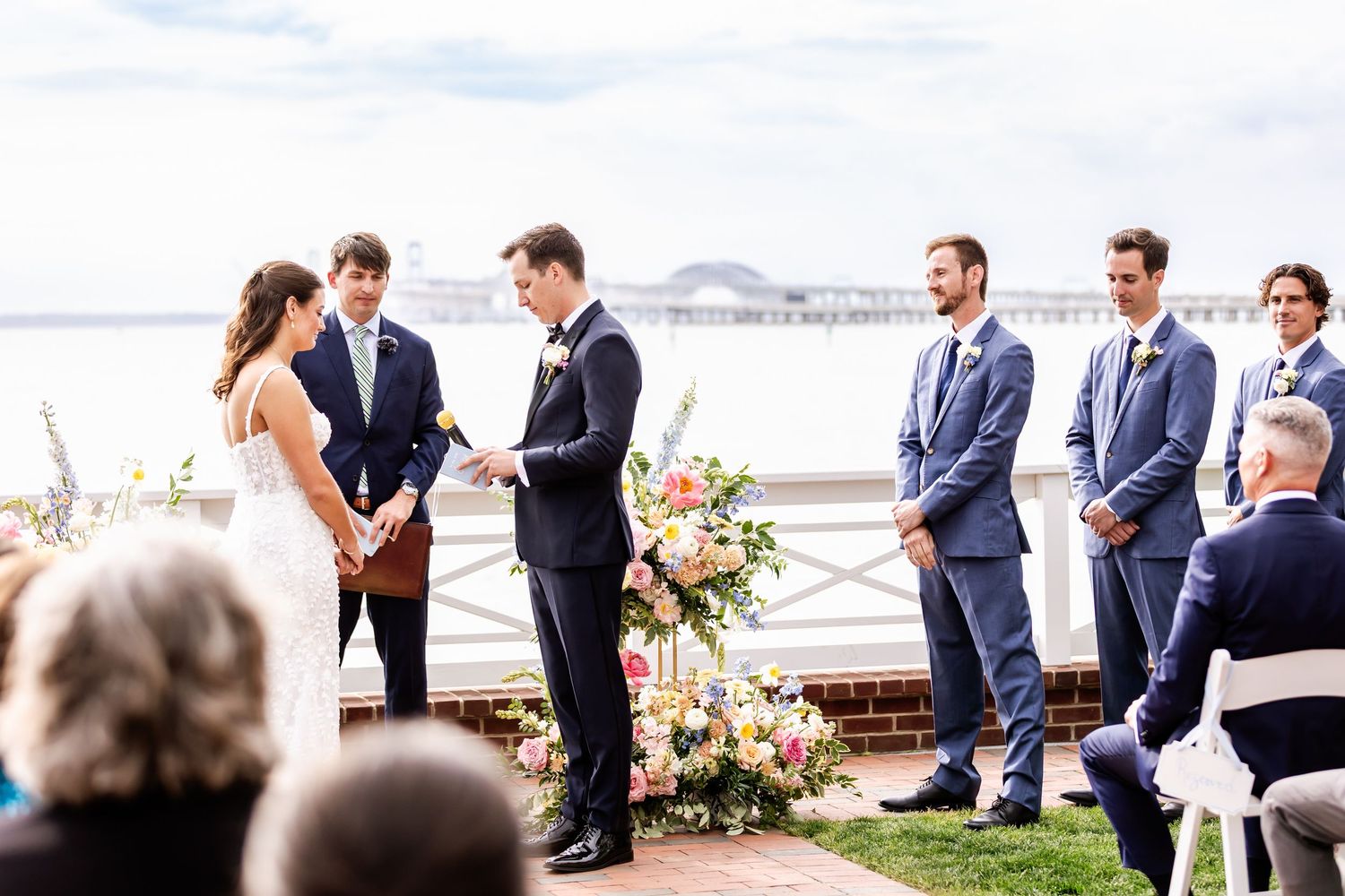 Outdoor waterfront wedding ceremony with floral arrangements and wedding party.