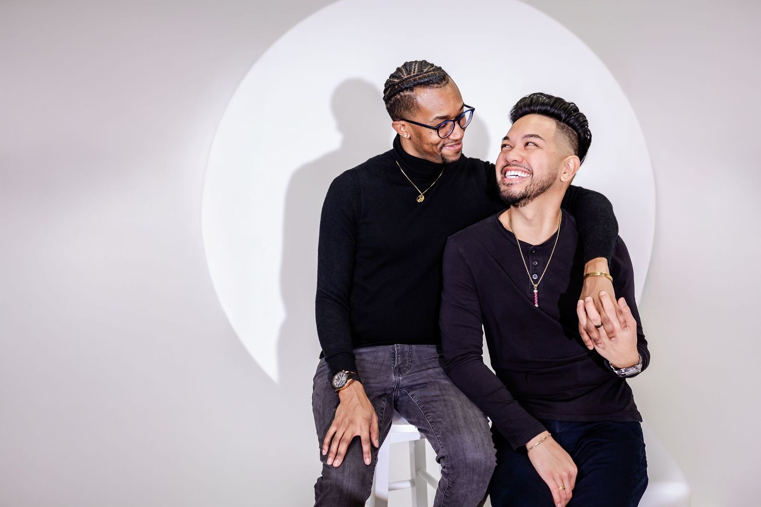 Two people in dark clothing pose intimately against a light circular backdrop.