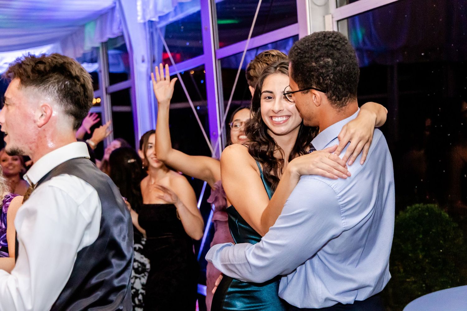 Wedding guests dancing and celebrating under purple mood lighting at an evening reception.