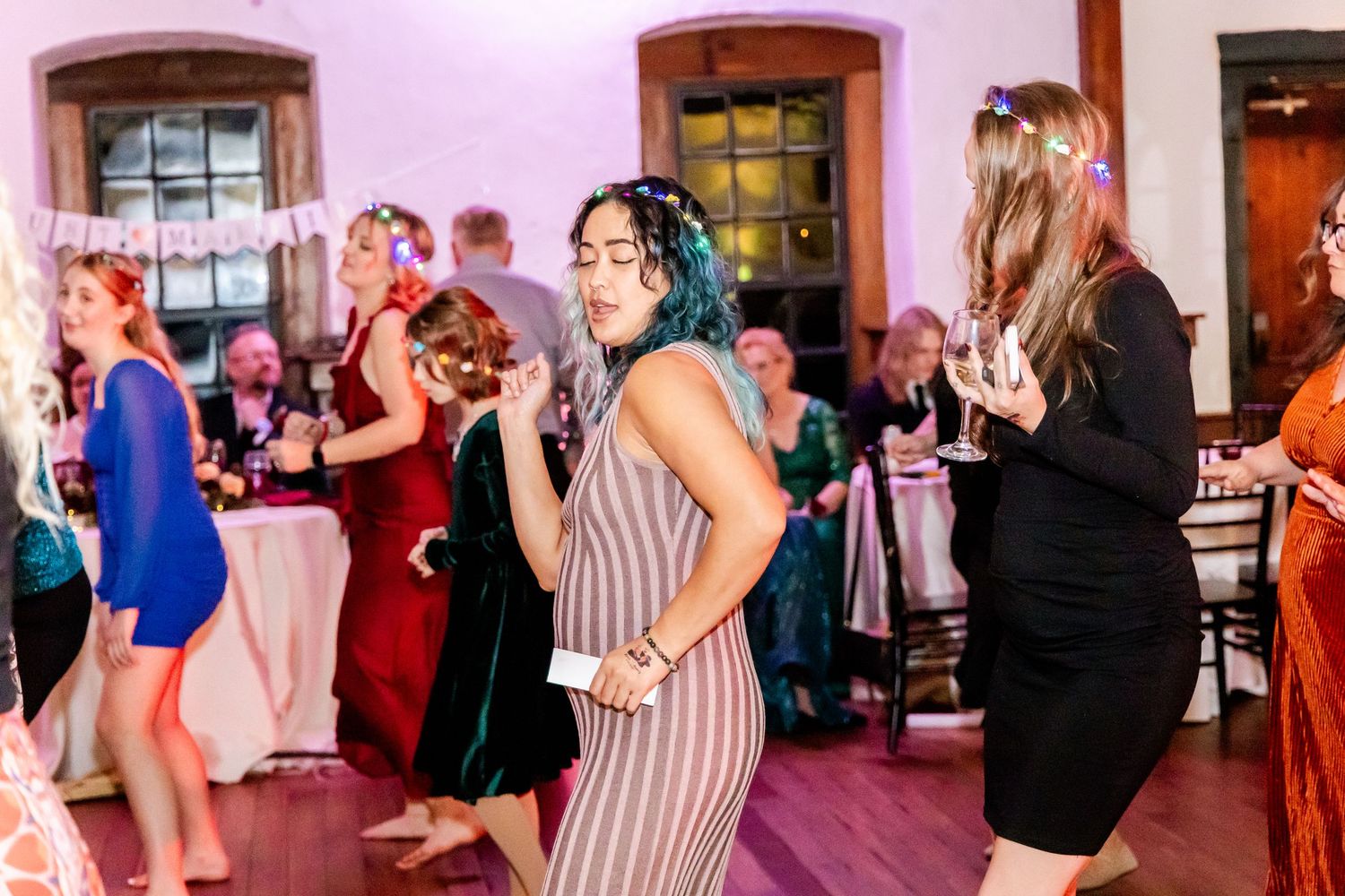 Wedding reception dance floor filled with guests under pink ambient lighting.