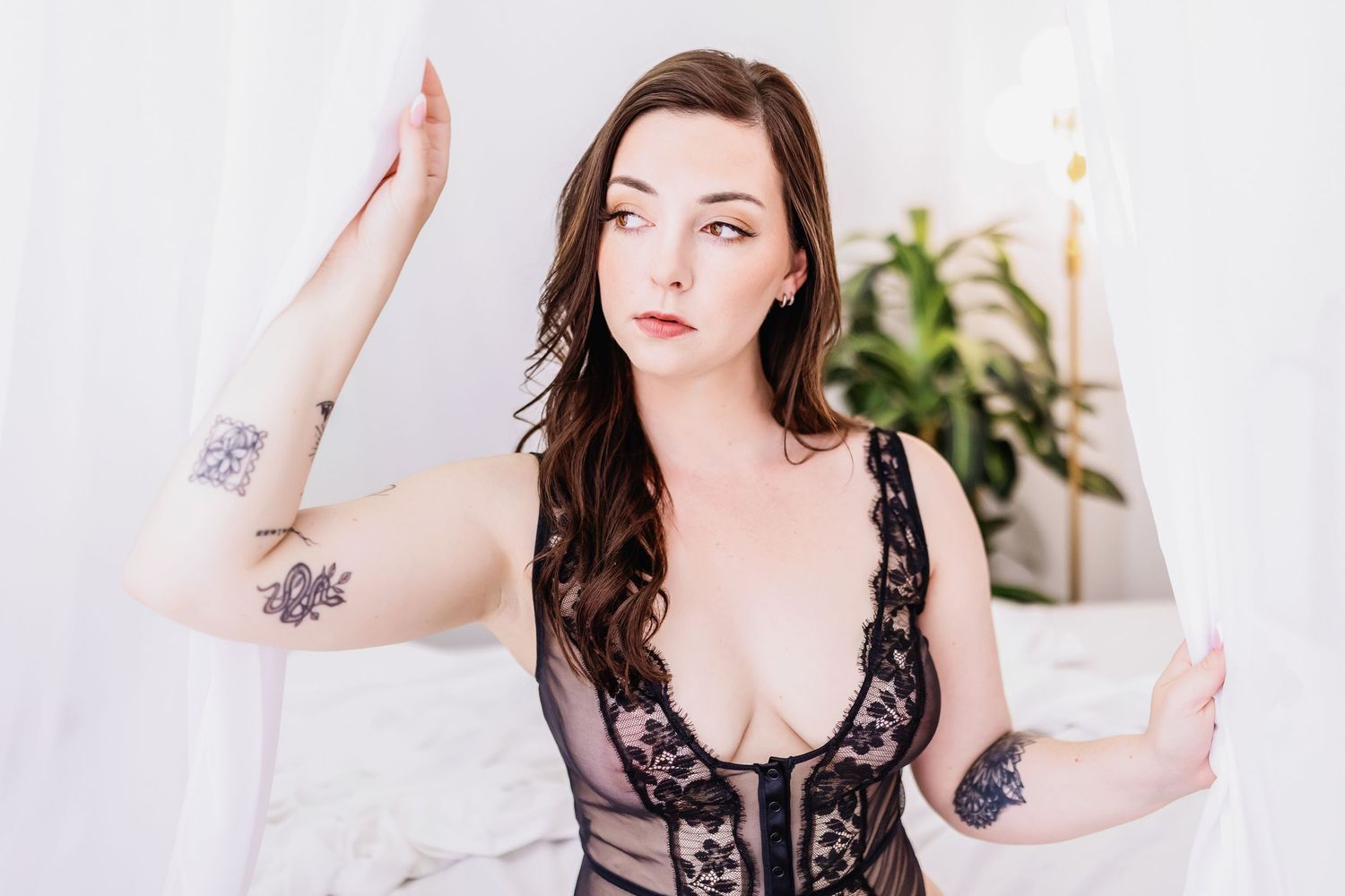 A boudoir photoshoot in a bright white room with natural light and green plants in the background.