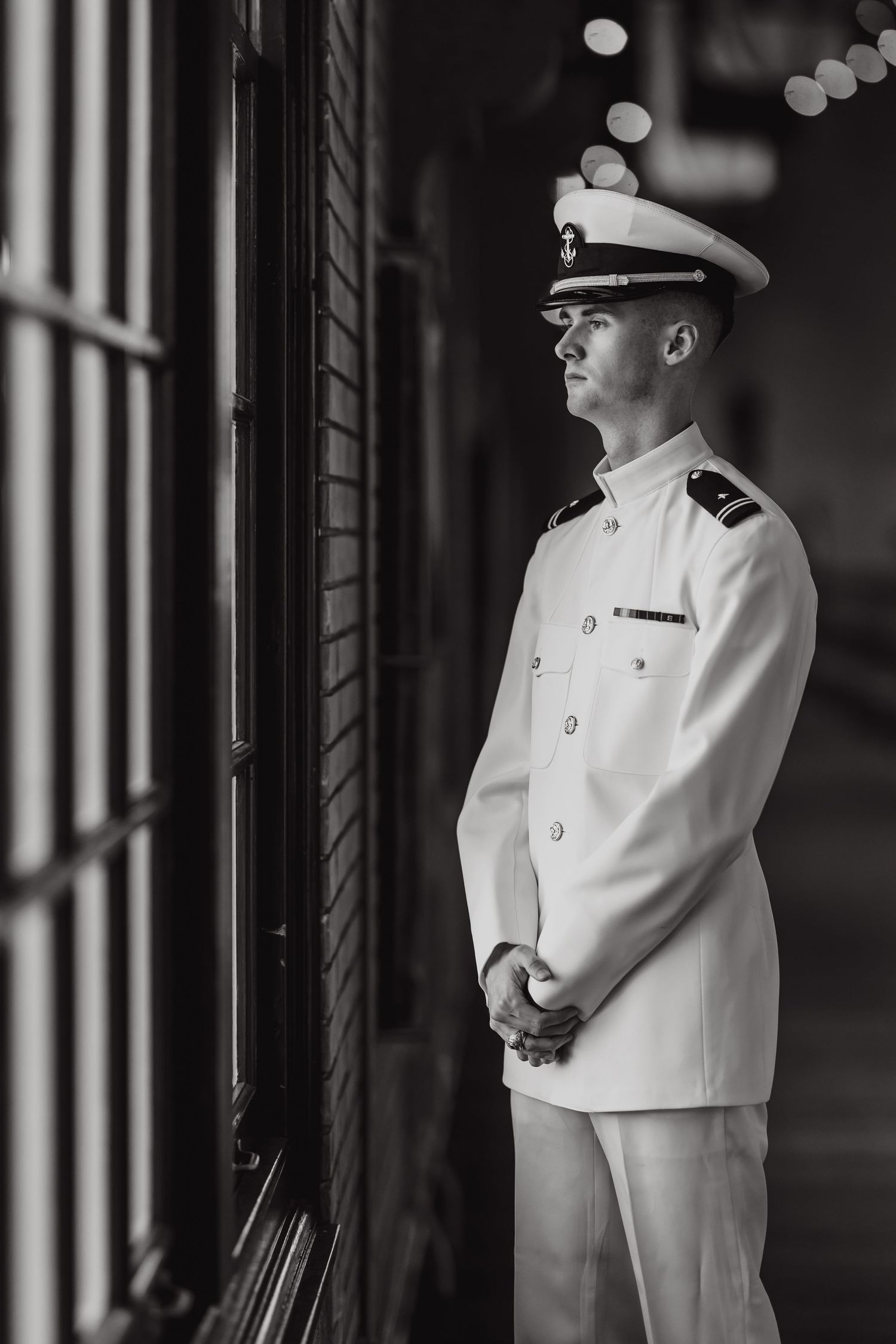 Black and white portrait of a naval officer in white dress uniform standing at attention near a window.