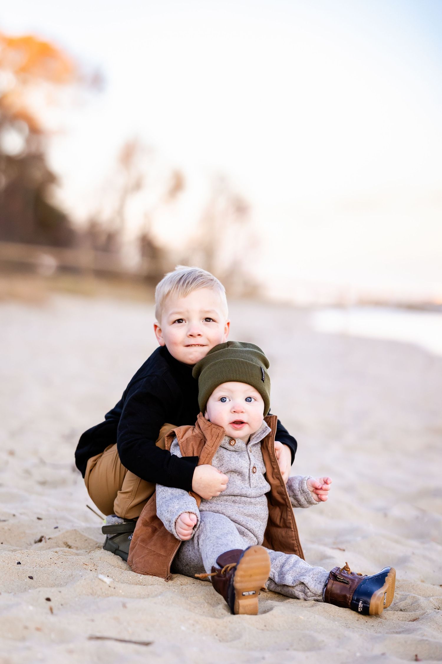A small child in gray clothing plays on a sandy beach at sunset while crawling and exploring the ground.