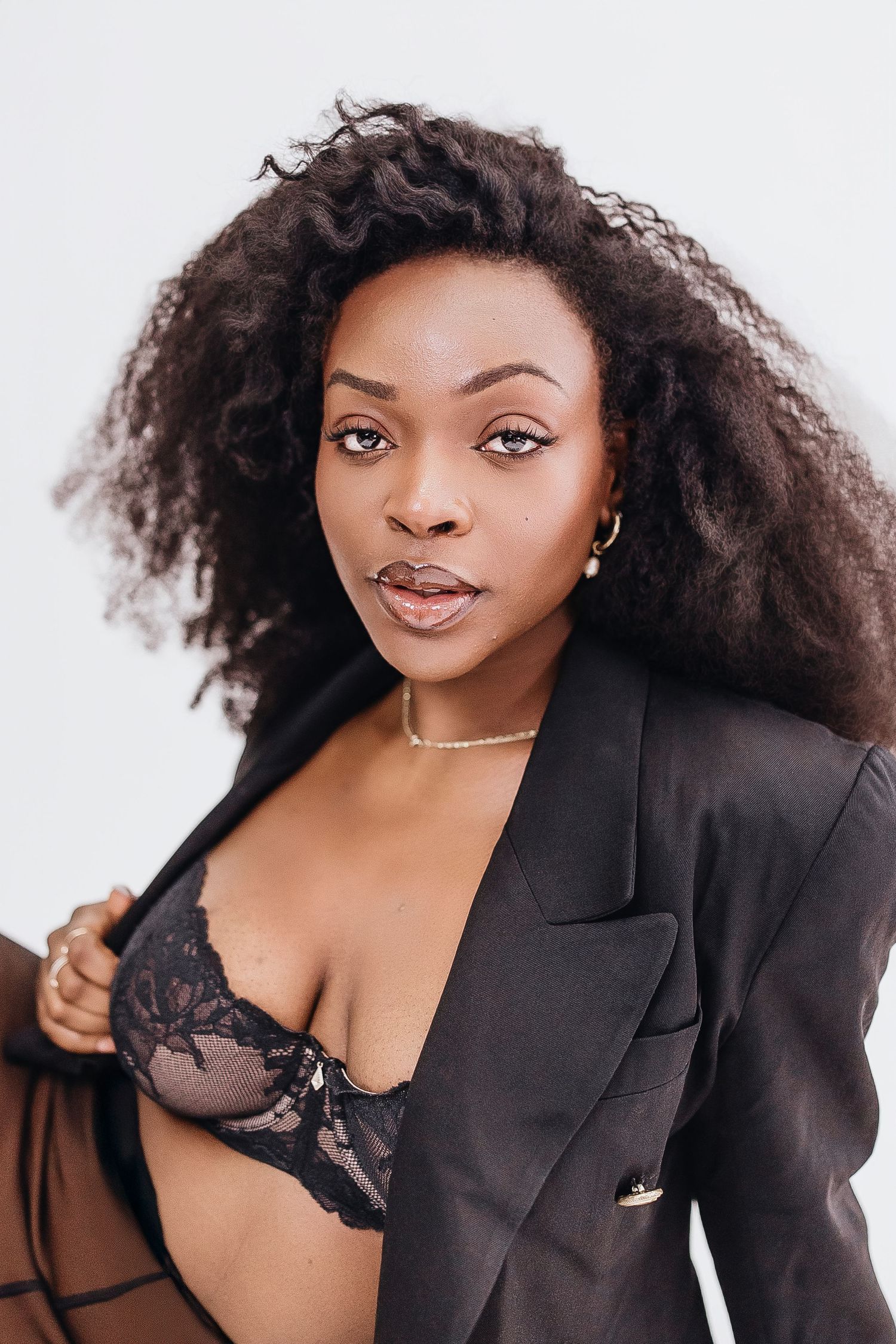 Fashion portrait series featuring model in black blazer and lingerie against white background with voluminous curly hair.