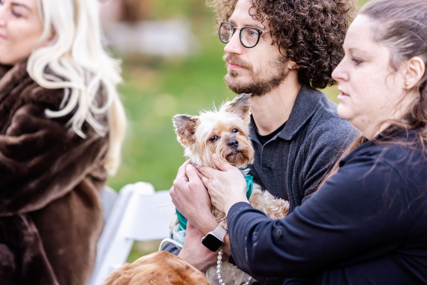 Wedding guests show emotional reactions while watching outdoor ceremony.