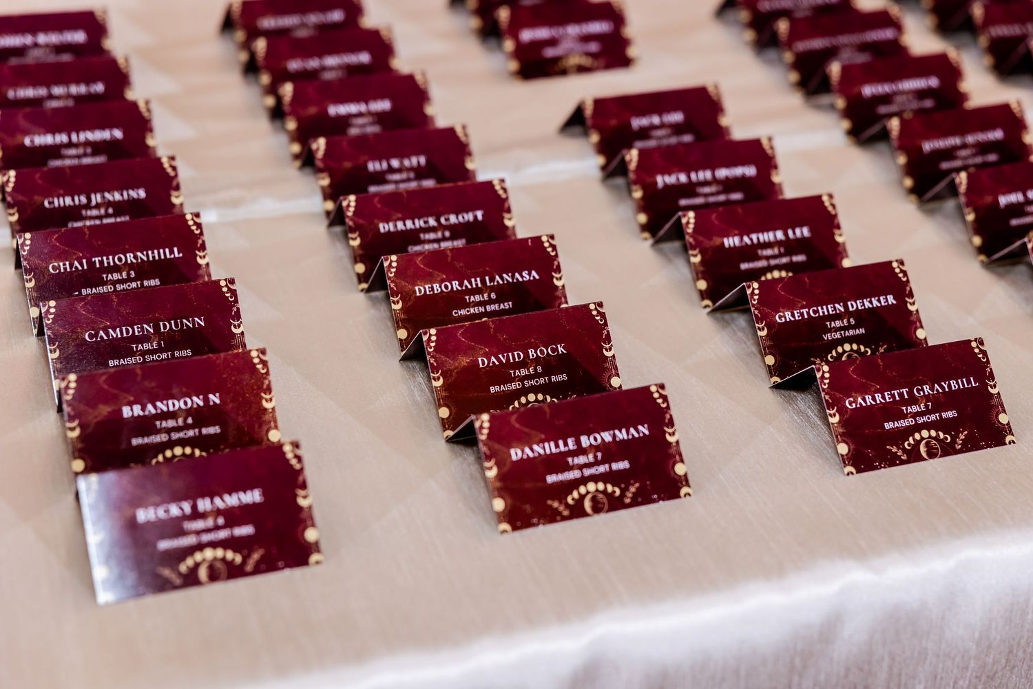 Rows of burgundy wedding place cards arranged neatly on a white tablecloth.
