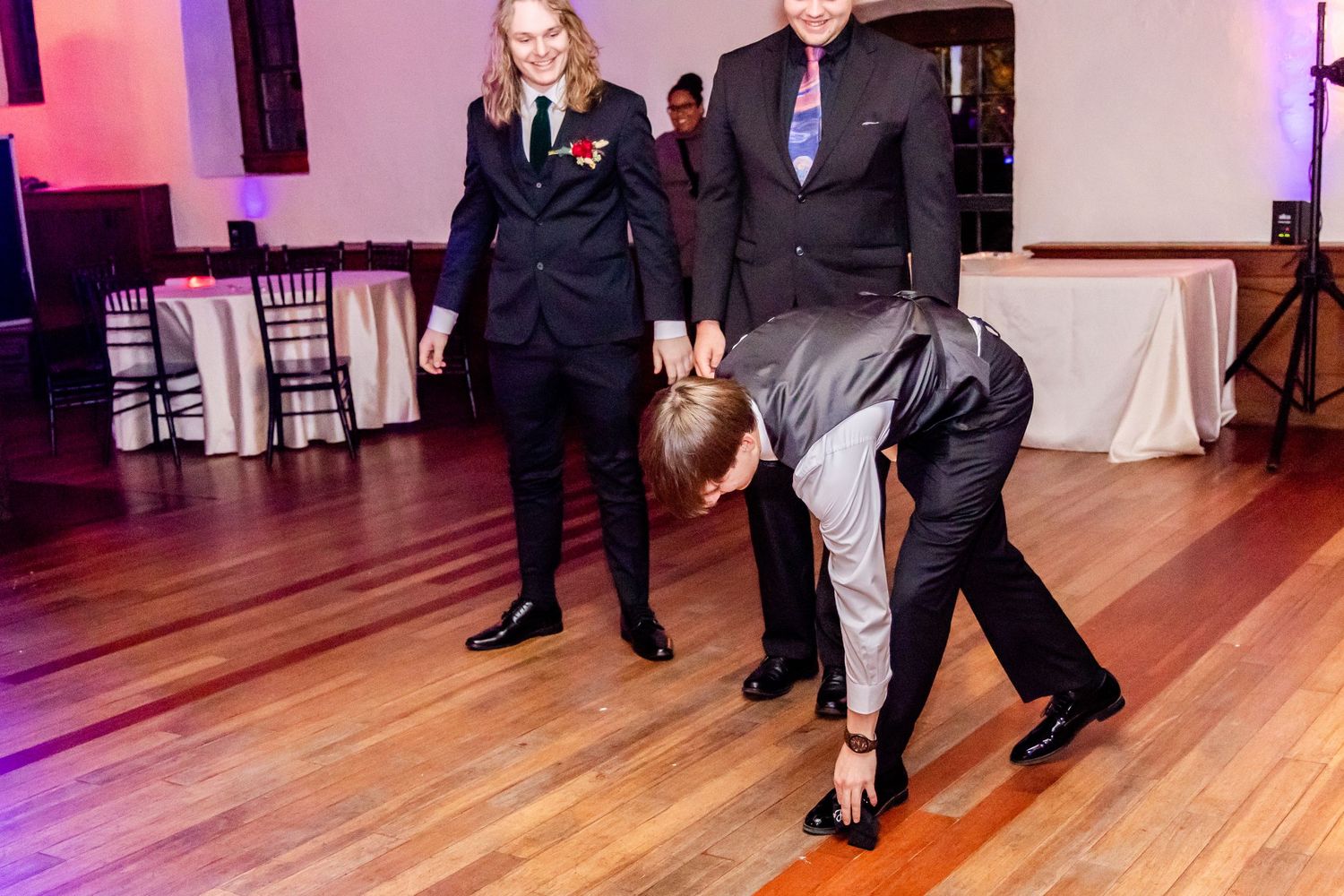 Wedding guests dancing and enjoying themselves on a hardwood floor with purple lighting.
