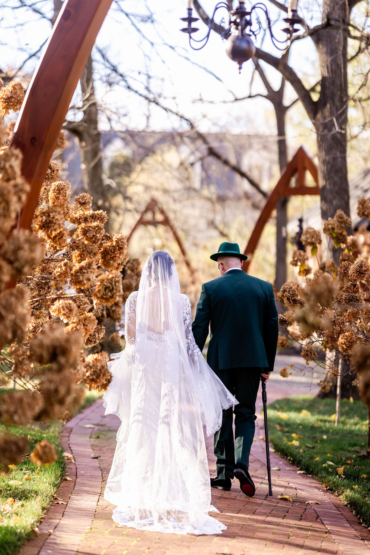 A couple walking along an autumn path with fallen leaves and trees during a wedding photo session.