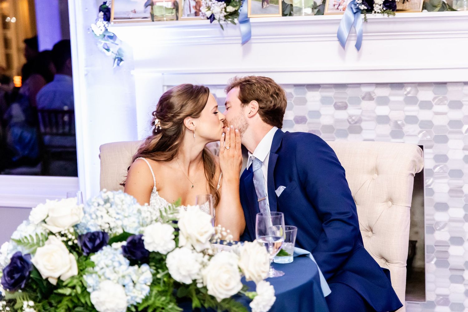 Wedding reception scene with white floral centerpieces and draped fabric ceiling.