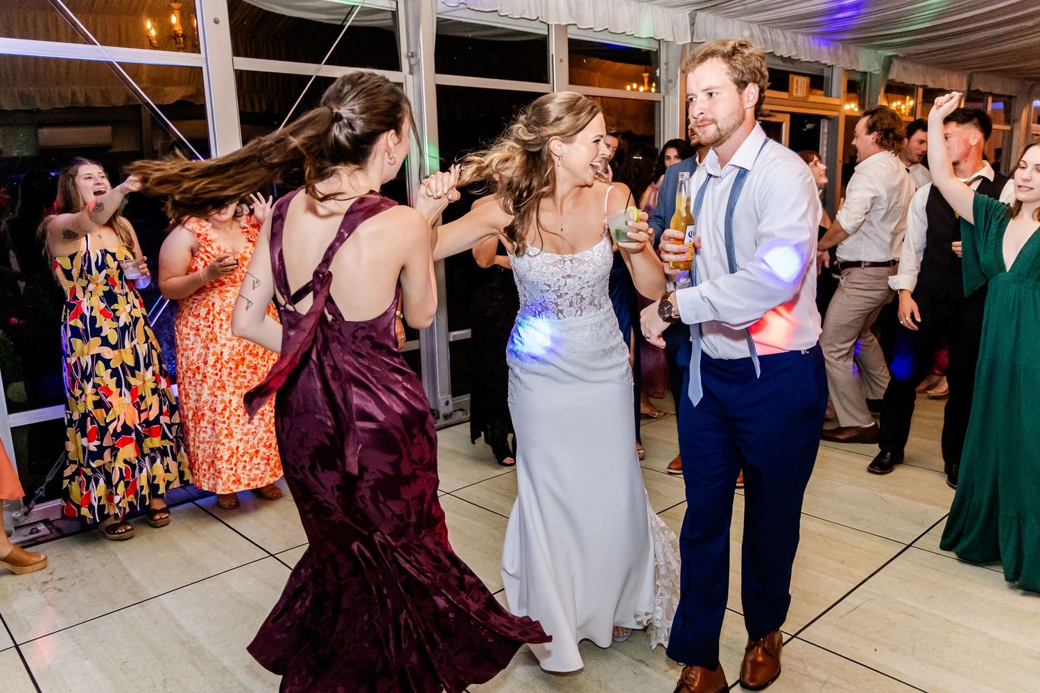 Wedding guests dance and celebrate on the dance floor under atmospheric lighting.
