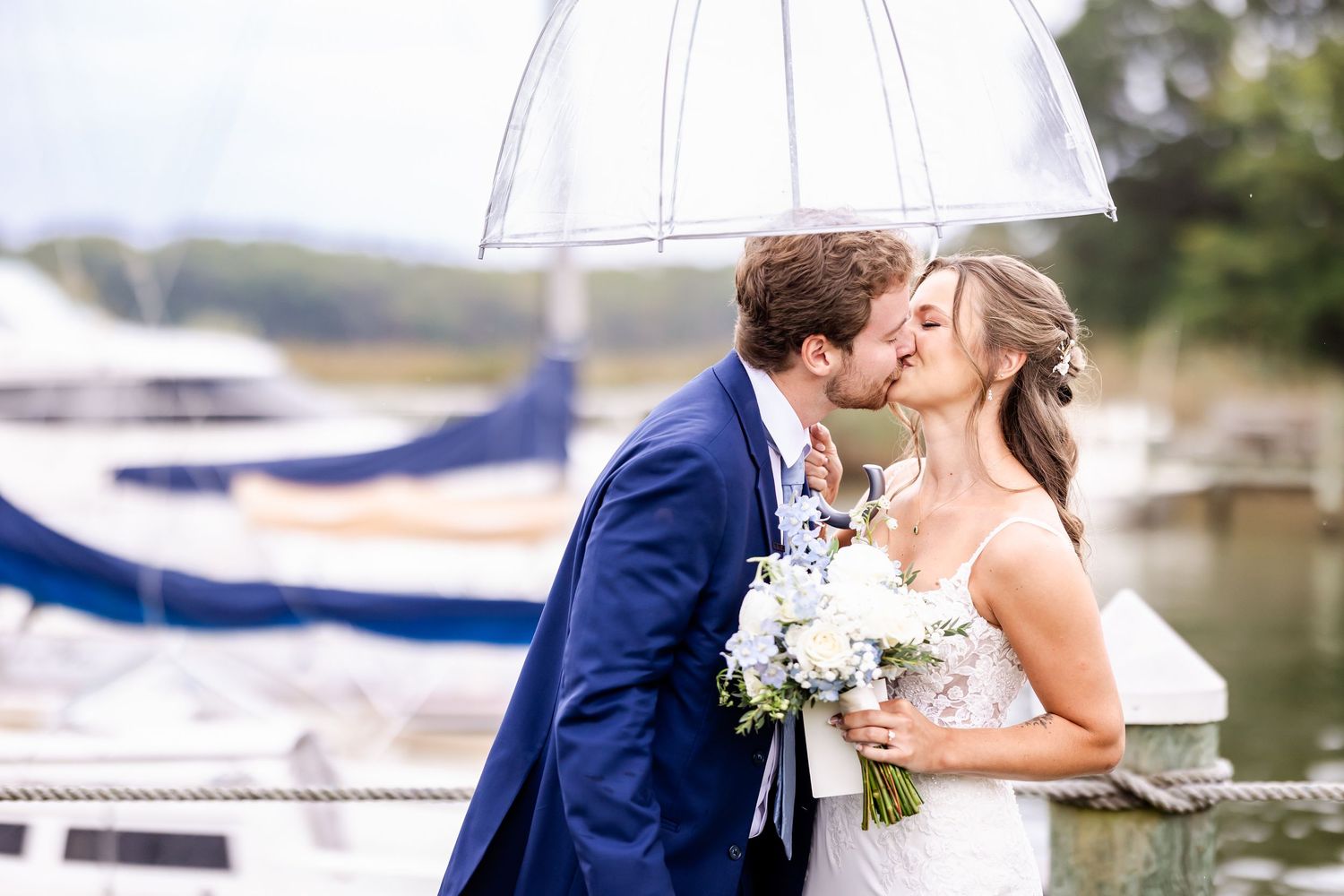 Wedding party shares joyful moments under a white umbrella by the marina.