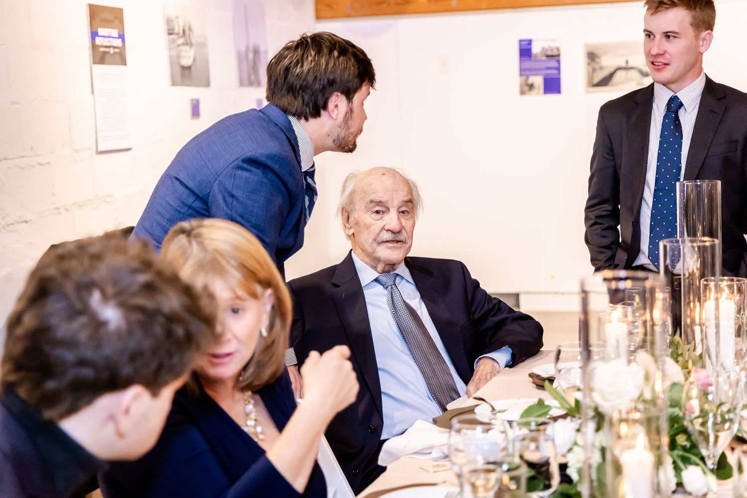 Elegant dinner gathering with guests seated at a decorated table, engaged in conversation in a formal dining setting.