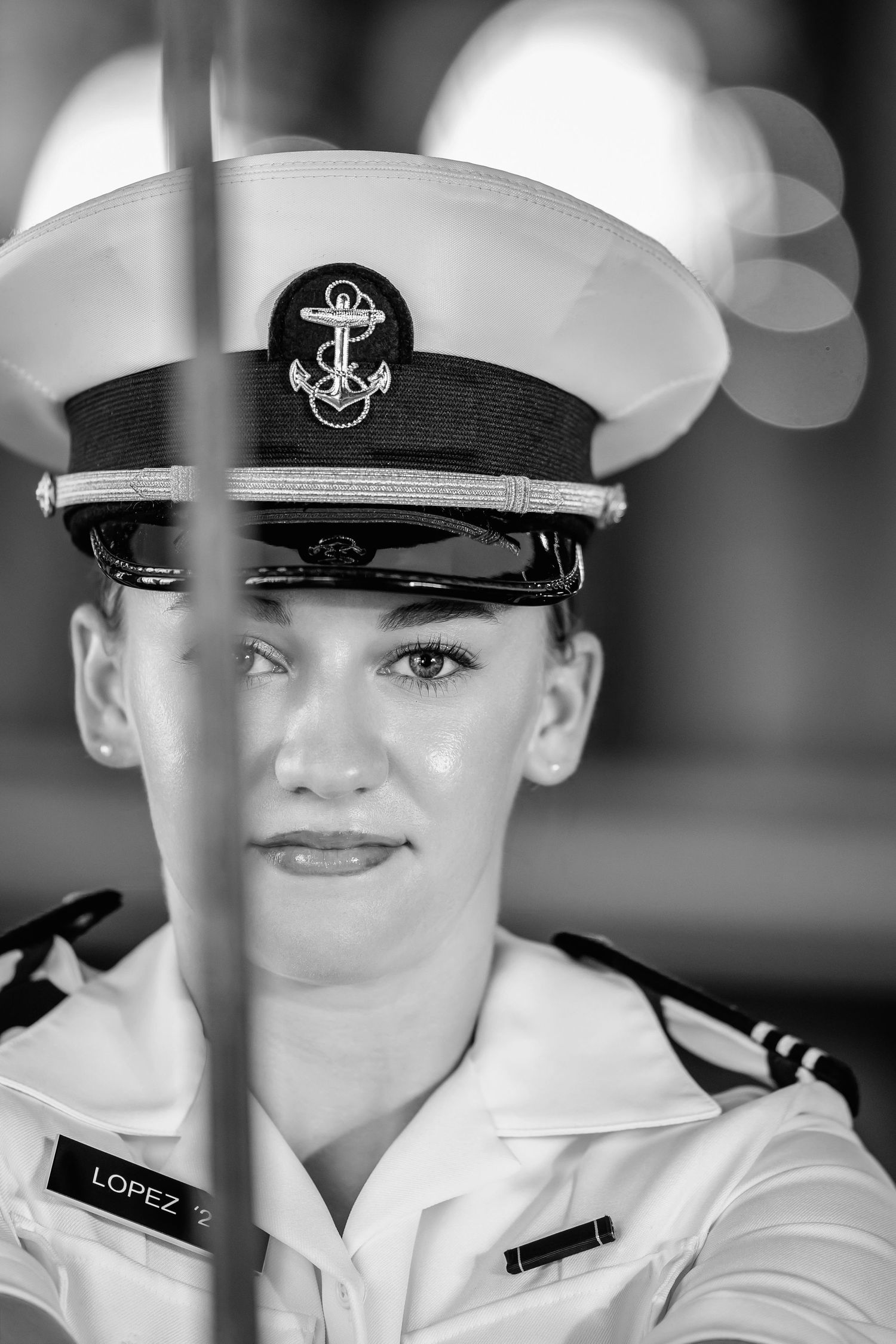 Black and white portrait of a young woman in a naval officer's white uniform and anchor-emblem cap, with a name tag on her chest.