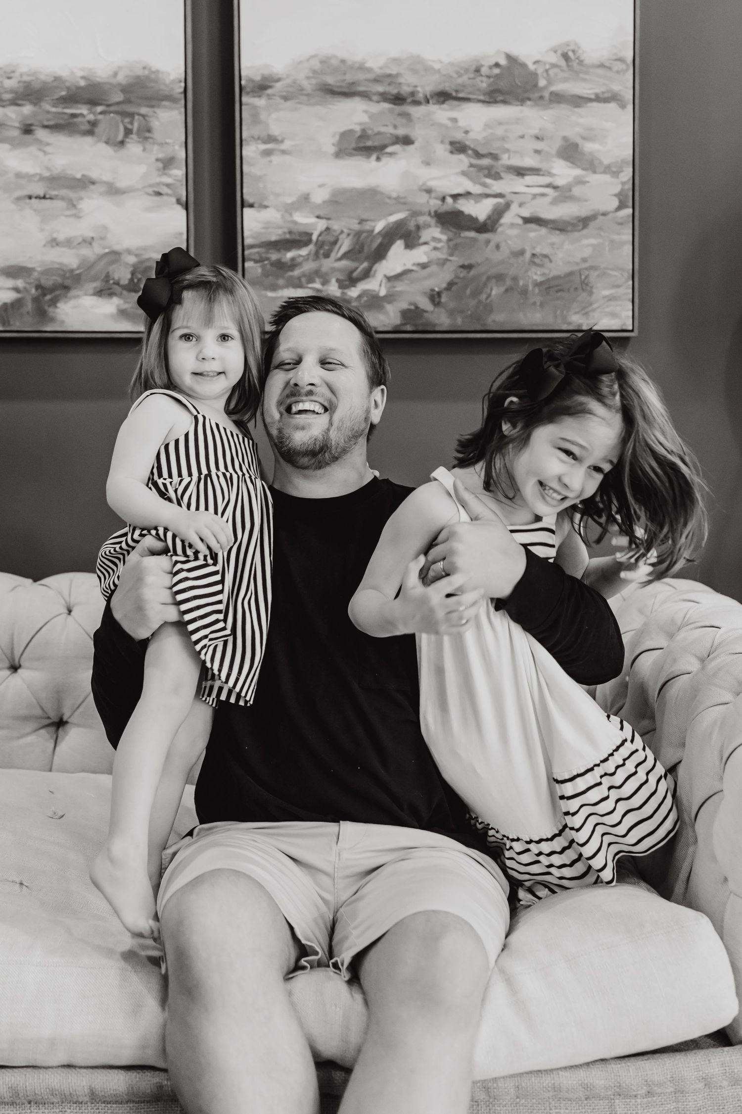 A joyful black and white family moment on a couch with a landscape painting hanging in the background.