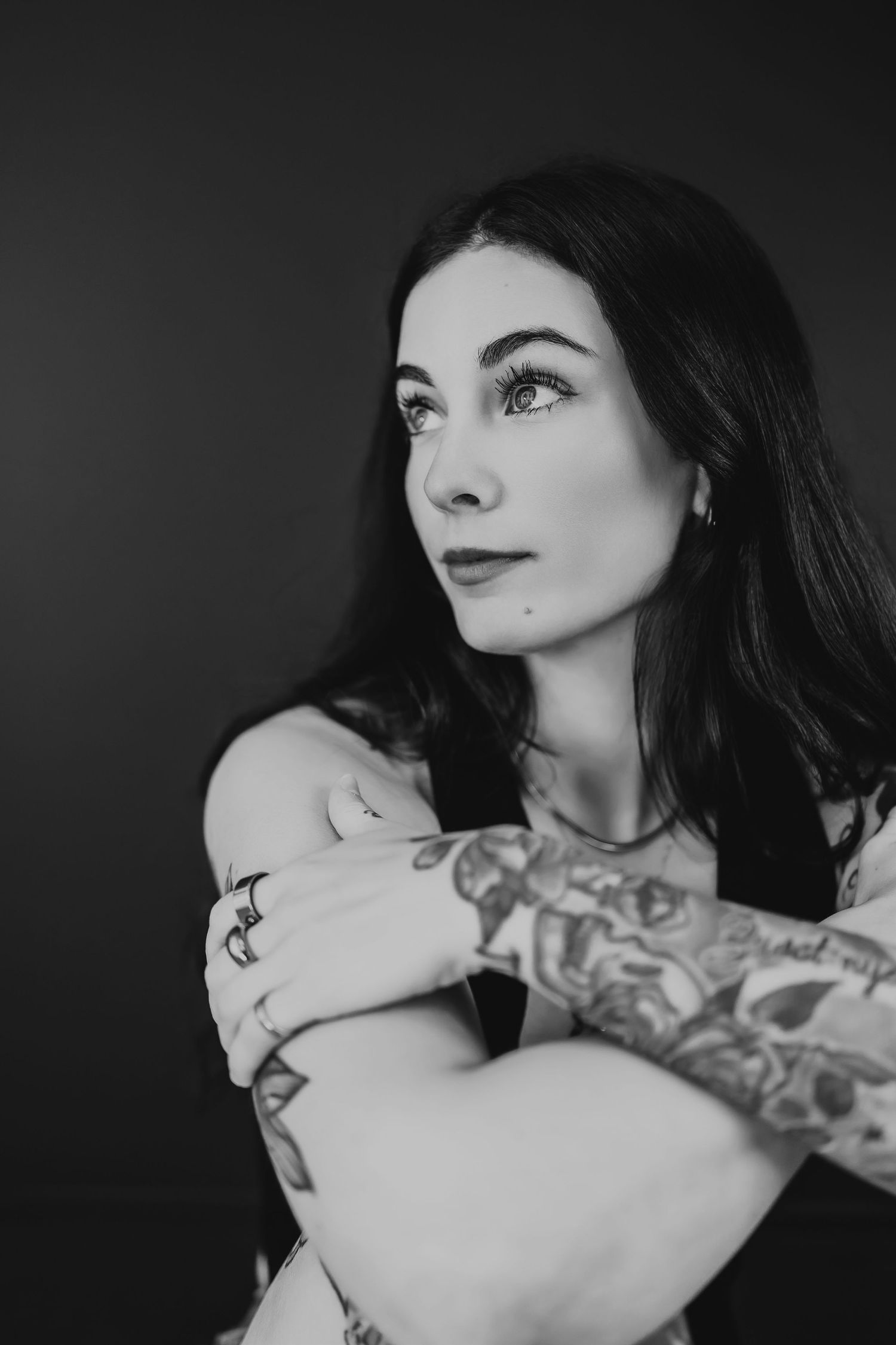 Dramatic black and white portrait showcasing artistic tattoos and elegant pose against dark background.