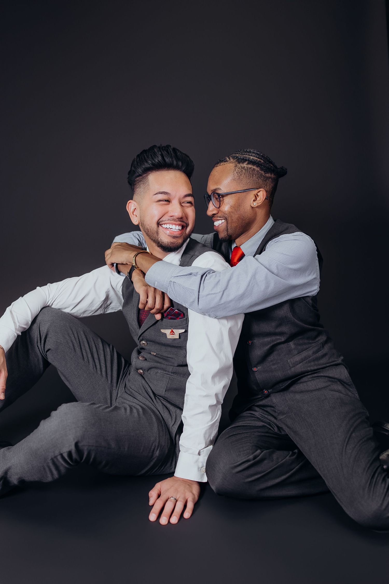Two people in contrasting outfits share a joyful moment while reclining on a dark surface.
