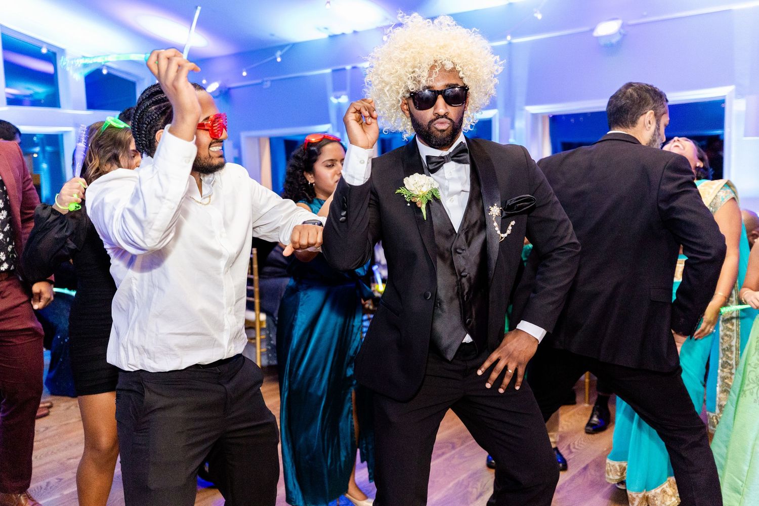 Wedding guests dance and celebrate on a blue-lit dance floor.