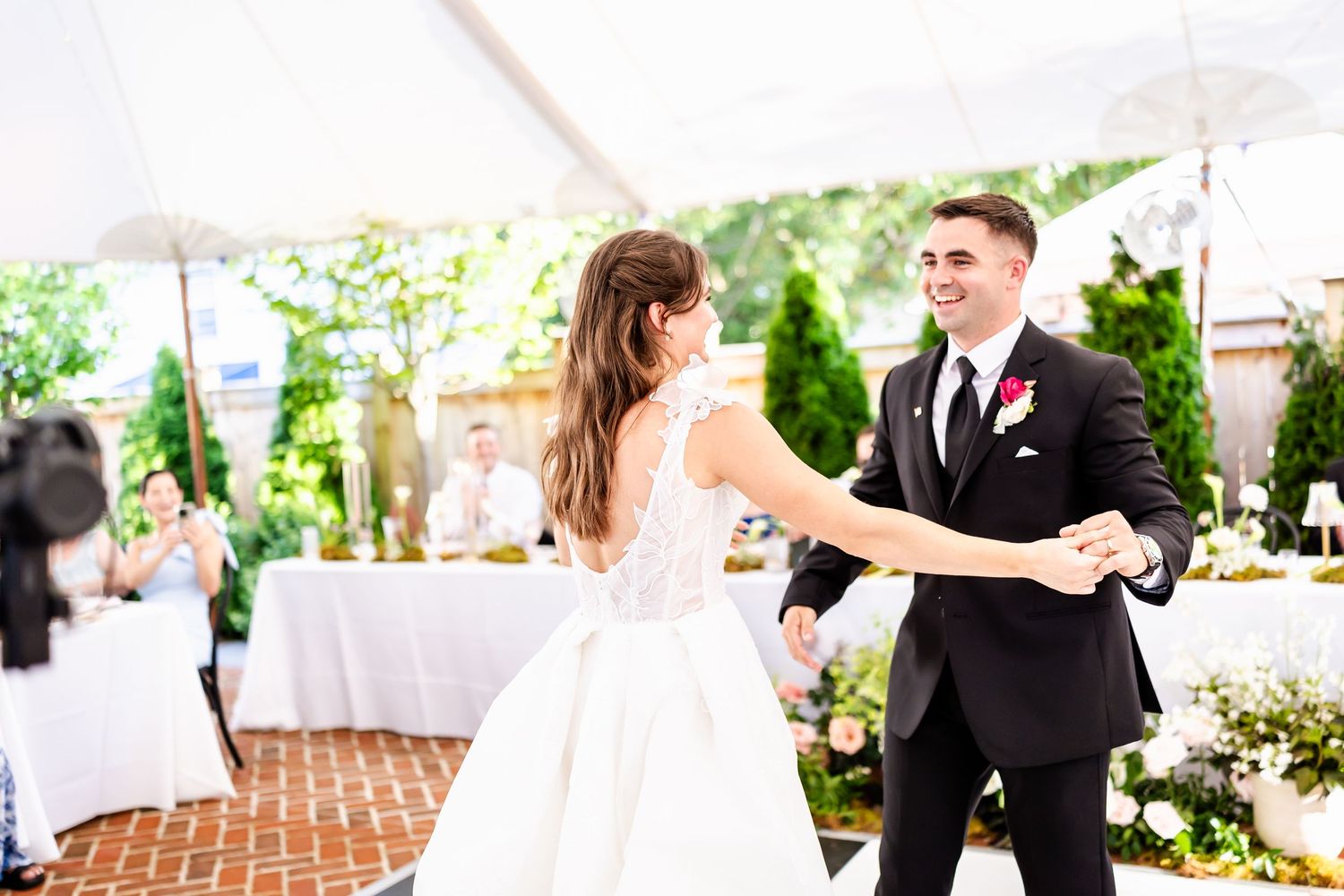 A wedding couple shares their first dance together on a patio surrounded by white reception tables and chairs.