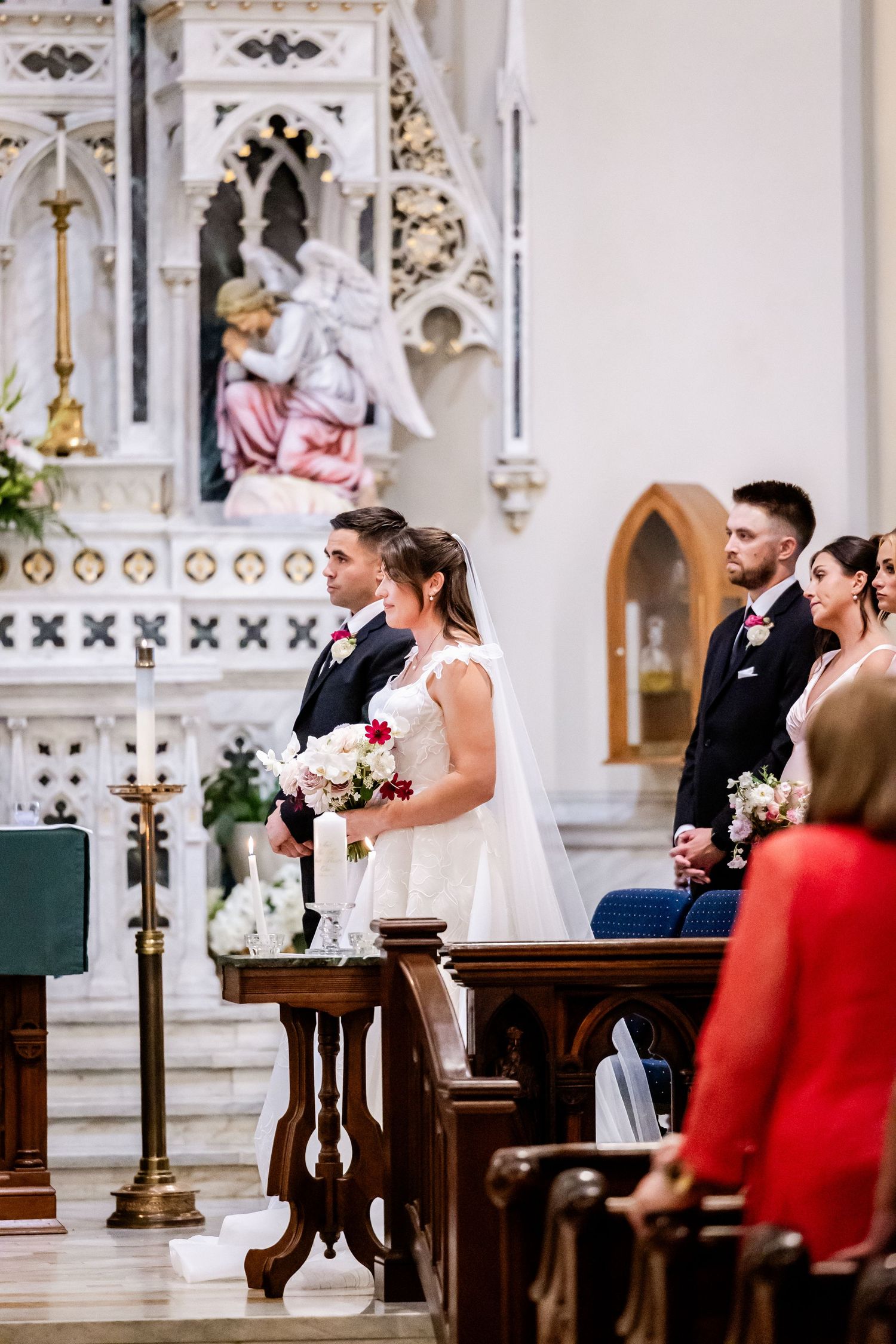 A wedding ceremony taking place inside an ornate Catholic church with decorative altar and white columns.