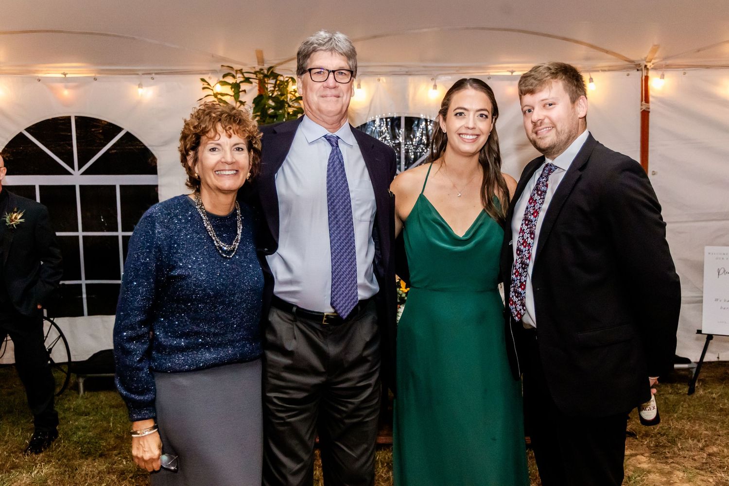 Wedding guests in formal attire posing together at an evening reception under a tent.