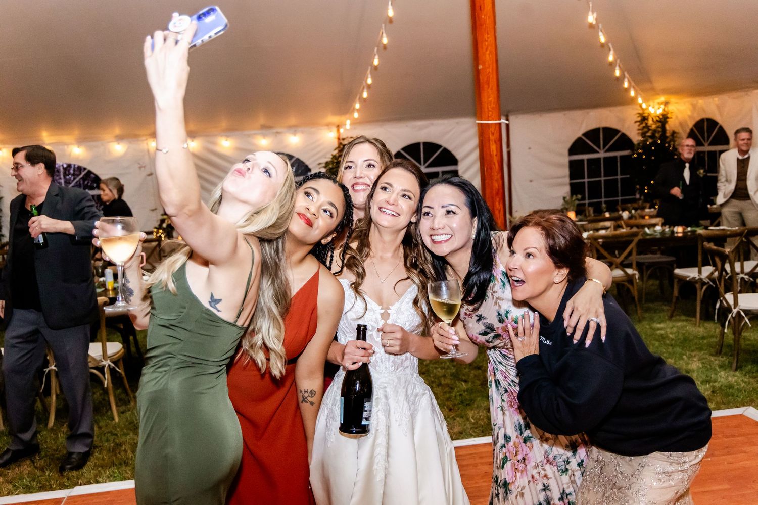 Wedding reception party scene with guests dancing under warm lighting and tent decor.
