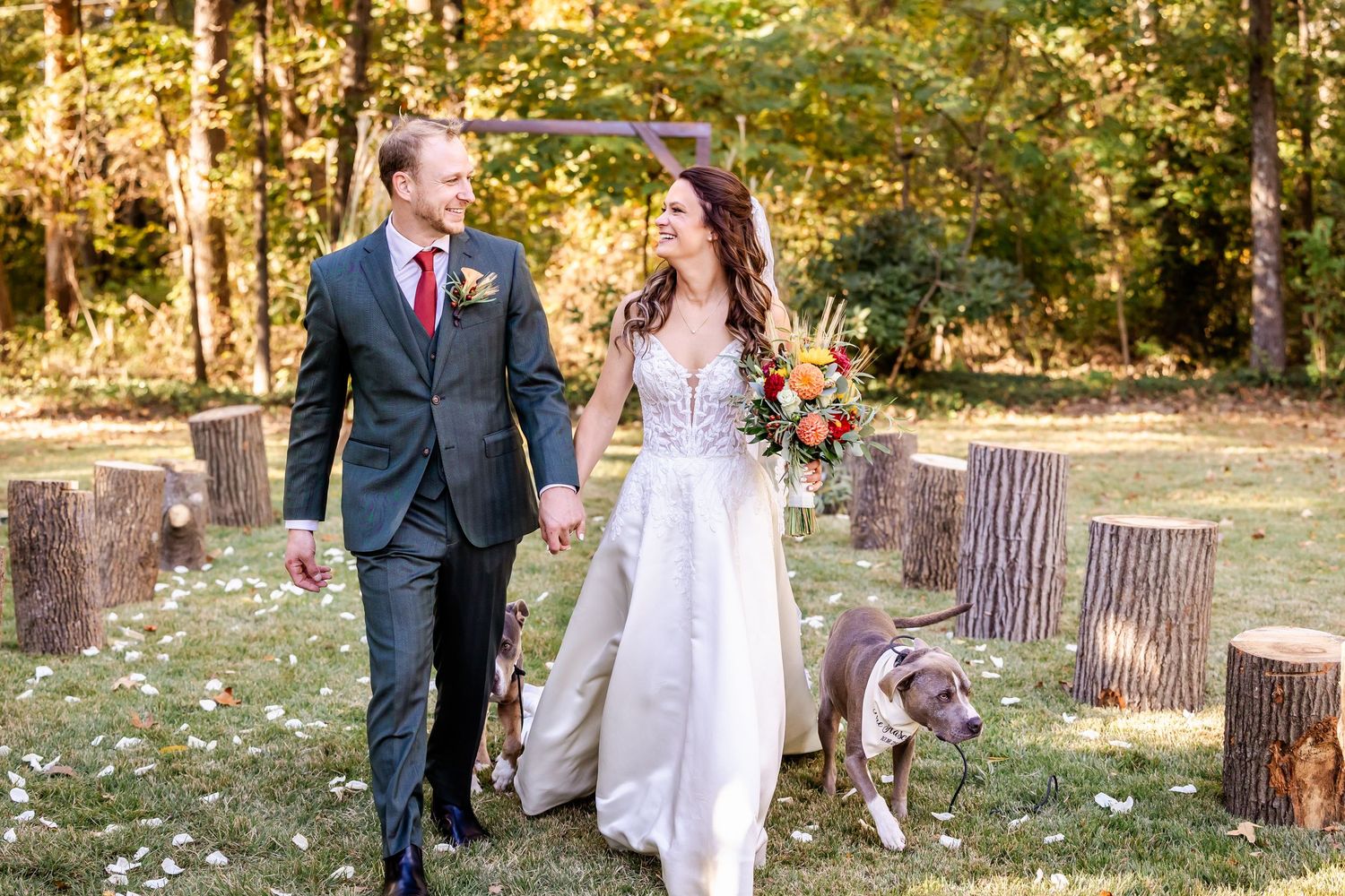 A couple walks their dog during their wedding photoshoot in a rustic outdoor setting.