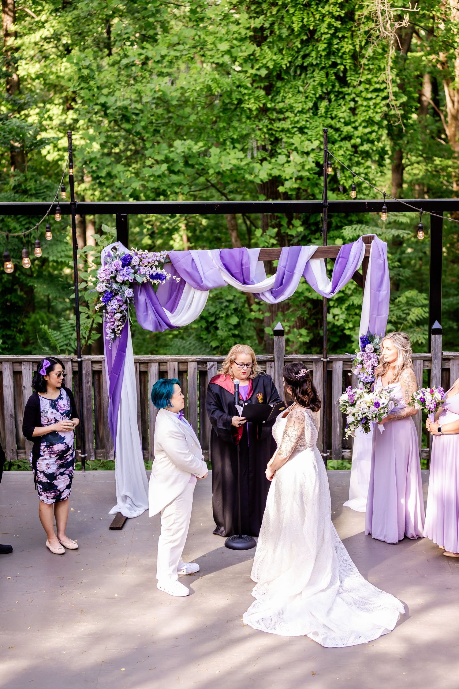 A wedding ceremony under a purple-decorated arch with attendants in coordinated attire.