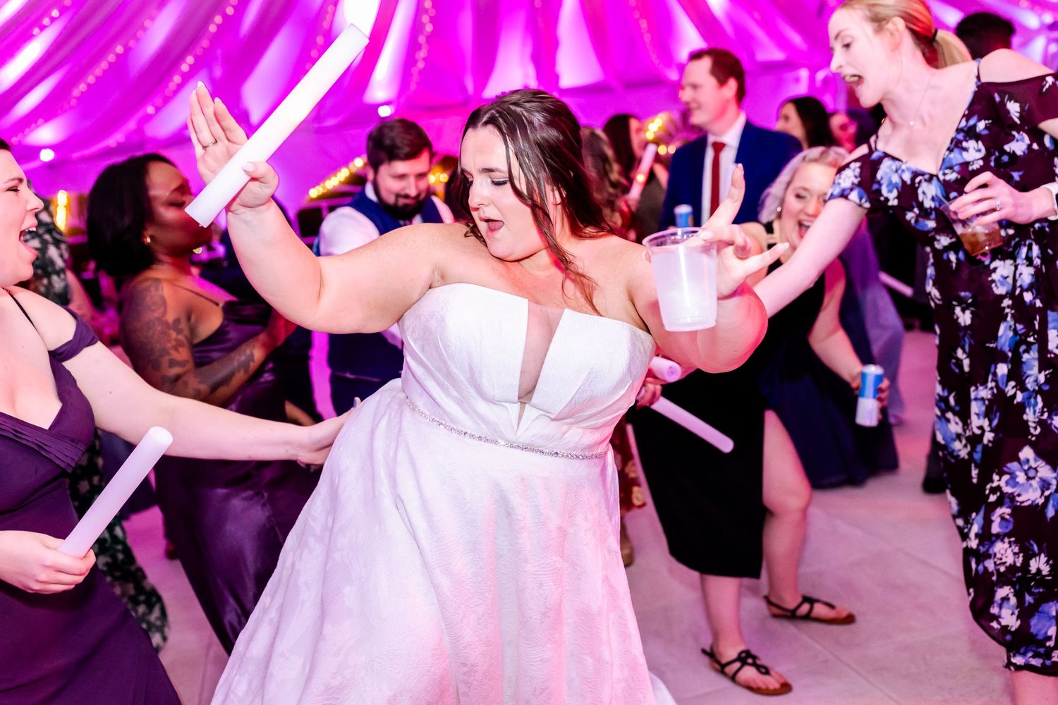 Wedding reception dance party with pink uplighting and ceiling draping.
