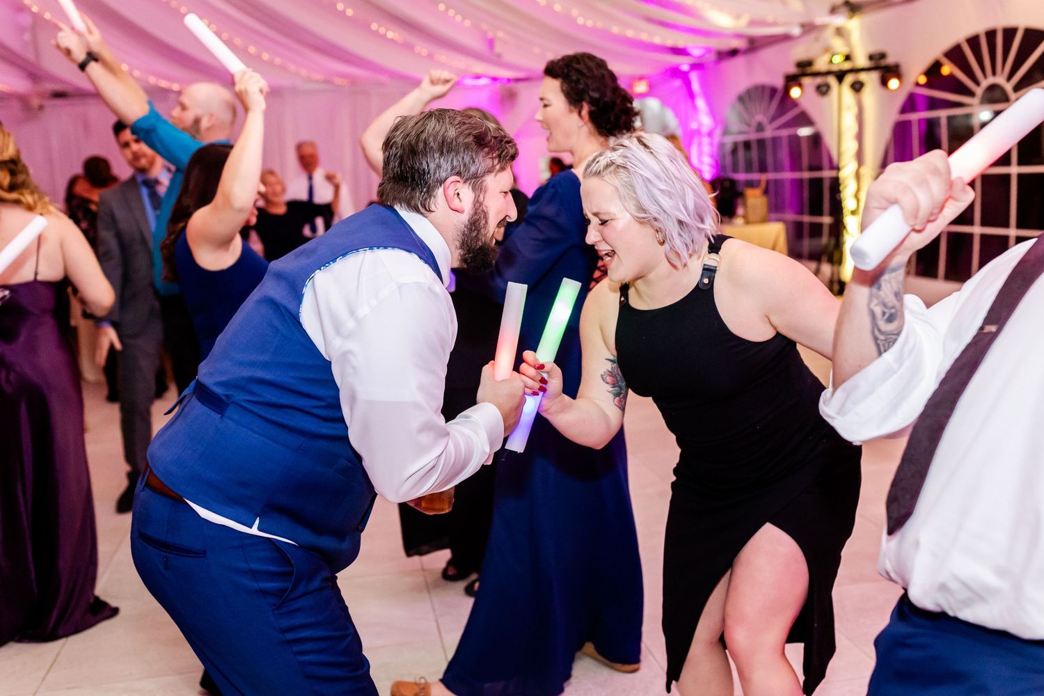 Energetic dancing scene at wedding reception under purple ambient lighting.