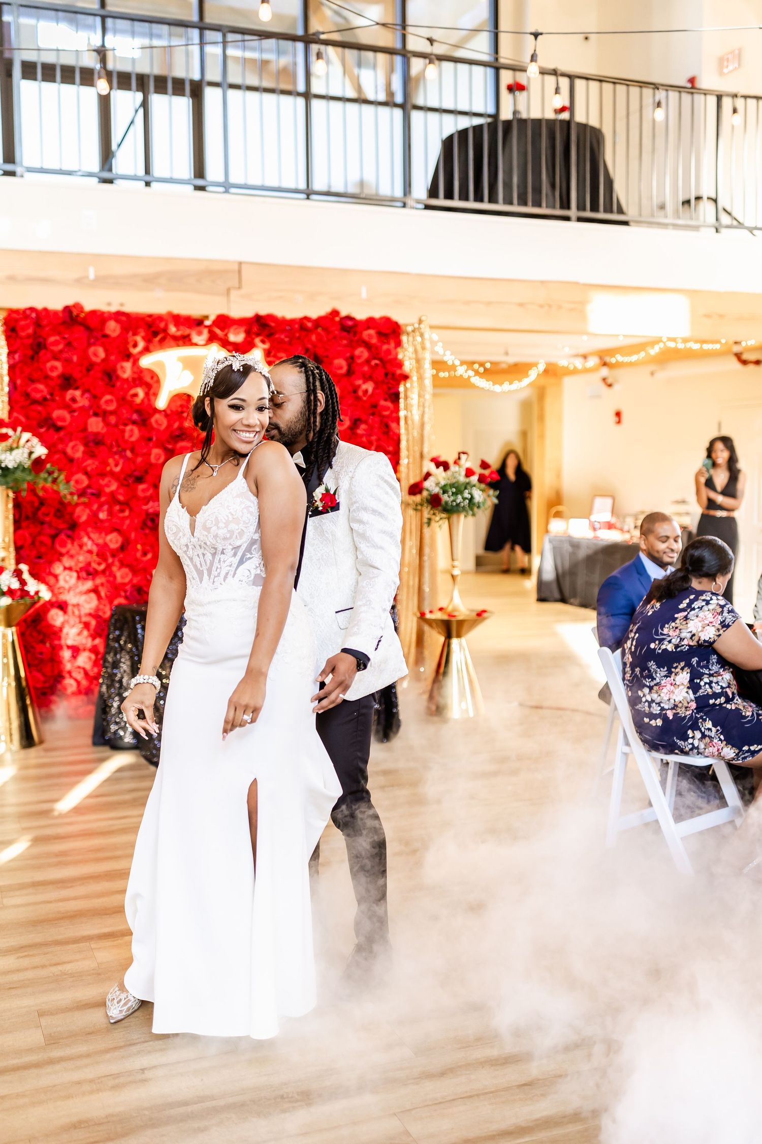 Wedding couple celebrating on dance floor with elegant red rose backdrop and atmospheric fog effects.