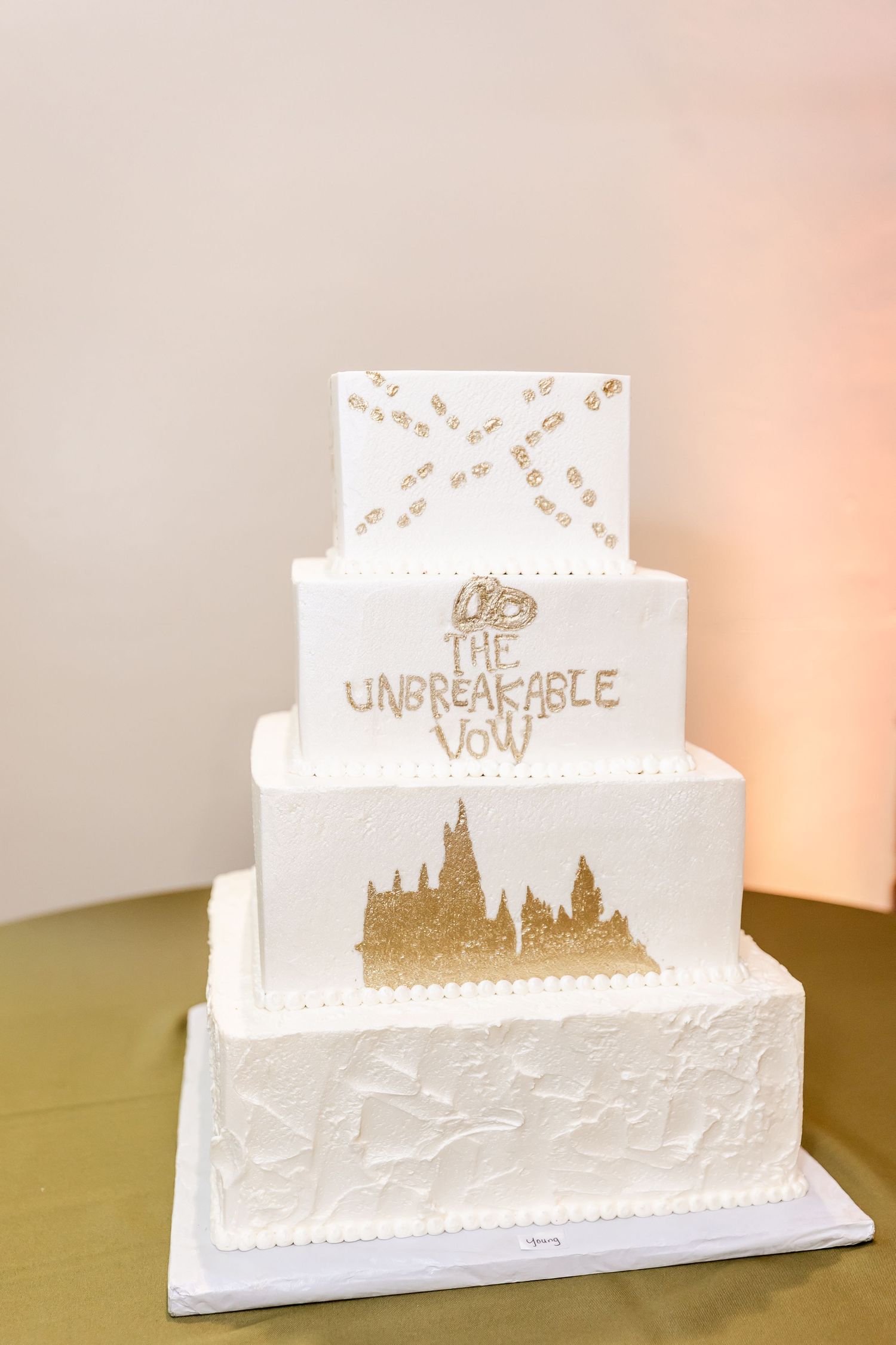 Four-tiered white wedding cake with gold accents and castle silhouette featuring Harry Potter themed design.