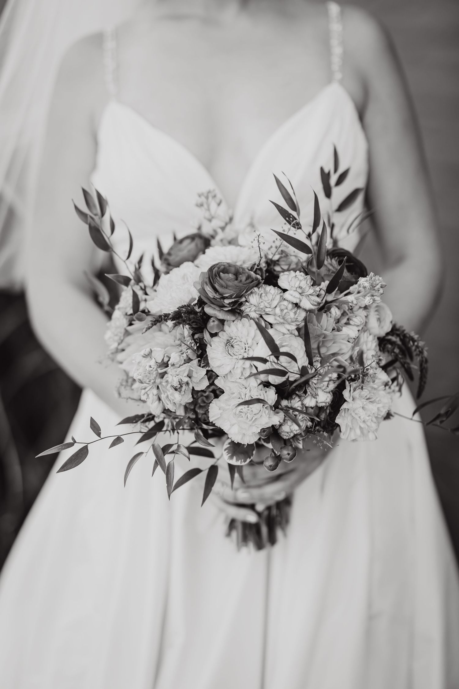 A black and white close-up of an elegant bridal bouquet with roses and delicate foliage.