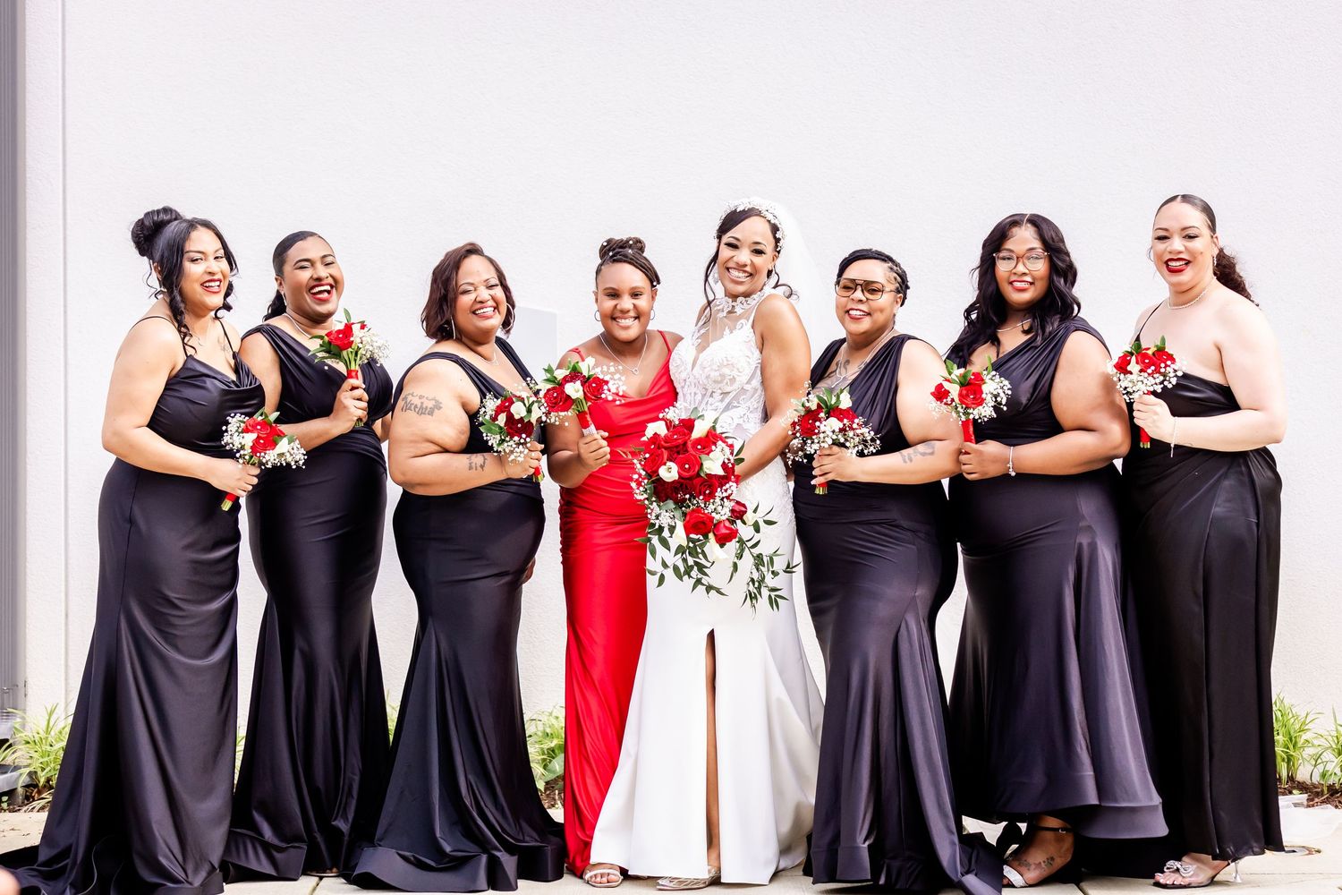 Wedding party in coordinated formal attire poses together with bouquets.