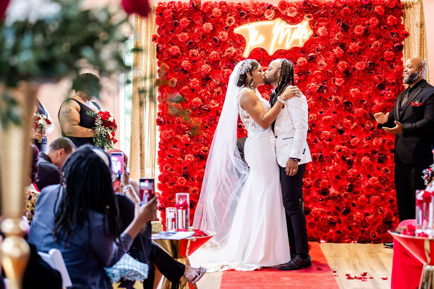Special moment captured during ceremony with stunning red flower wall background.