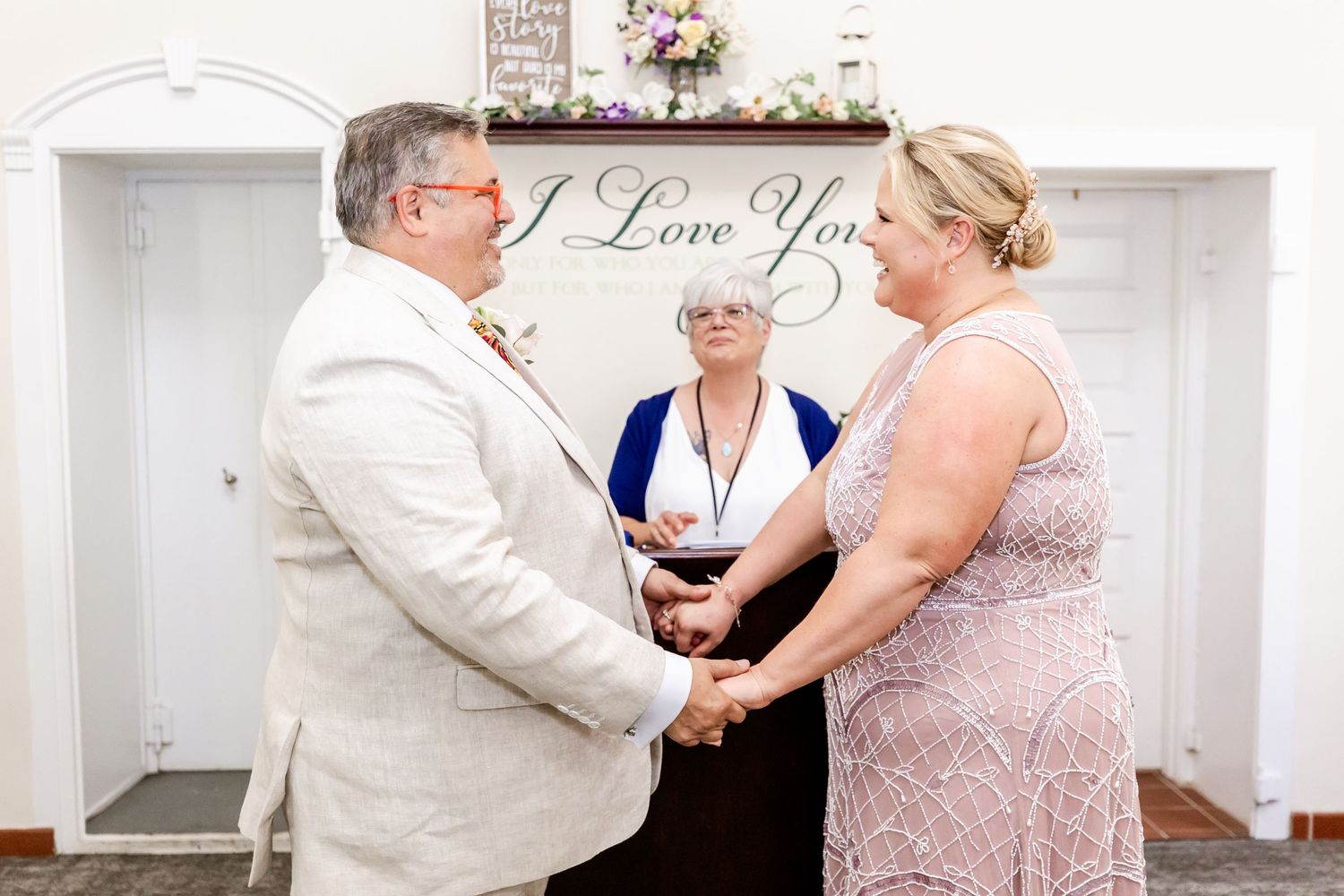 A ceremony takes place under a 'I Love You' sign in a white chapel setting.