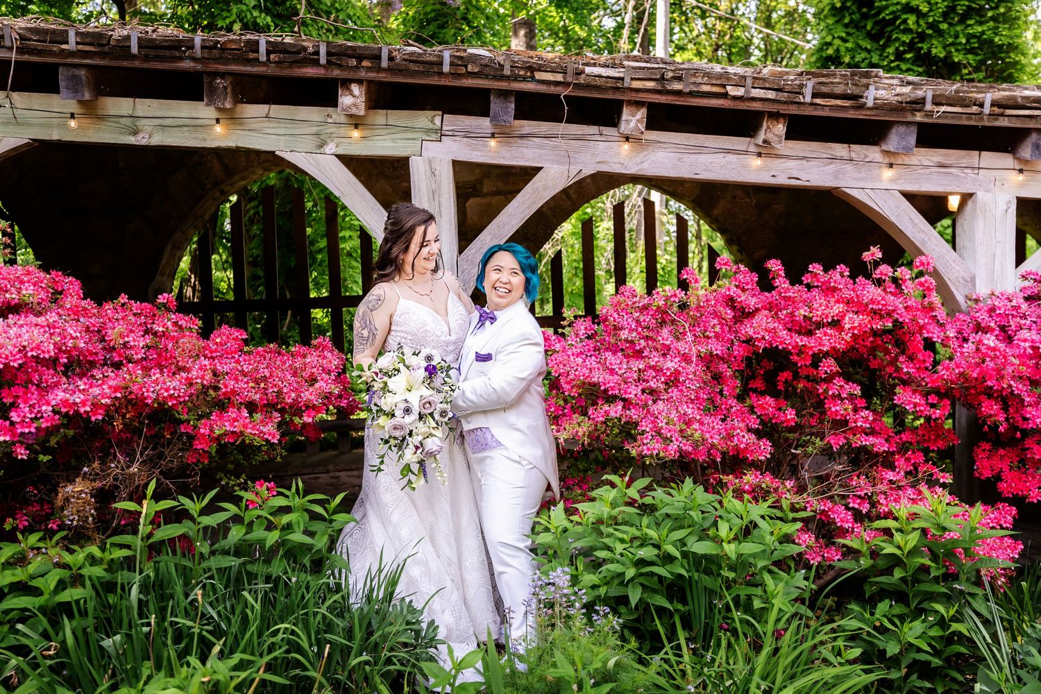 Beautiful spring wedding photo with vibrant pink azaleas and wooden pergola in the background.