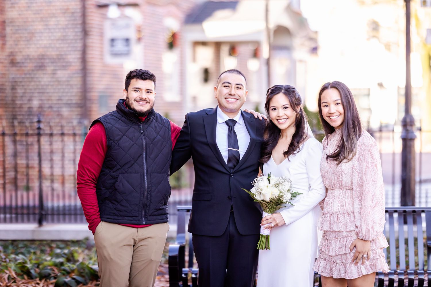 Group photo of wedding party outside brick building with iron fence in background.