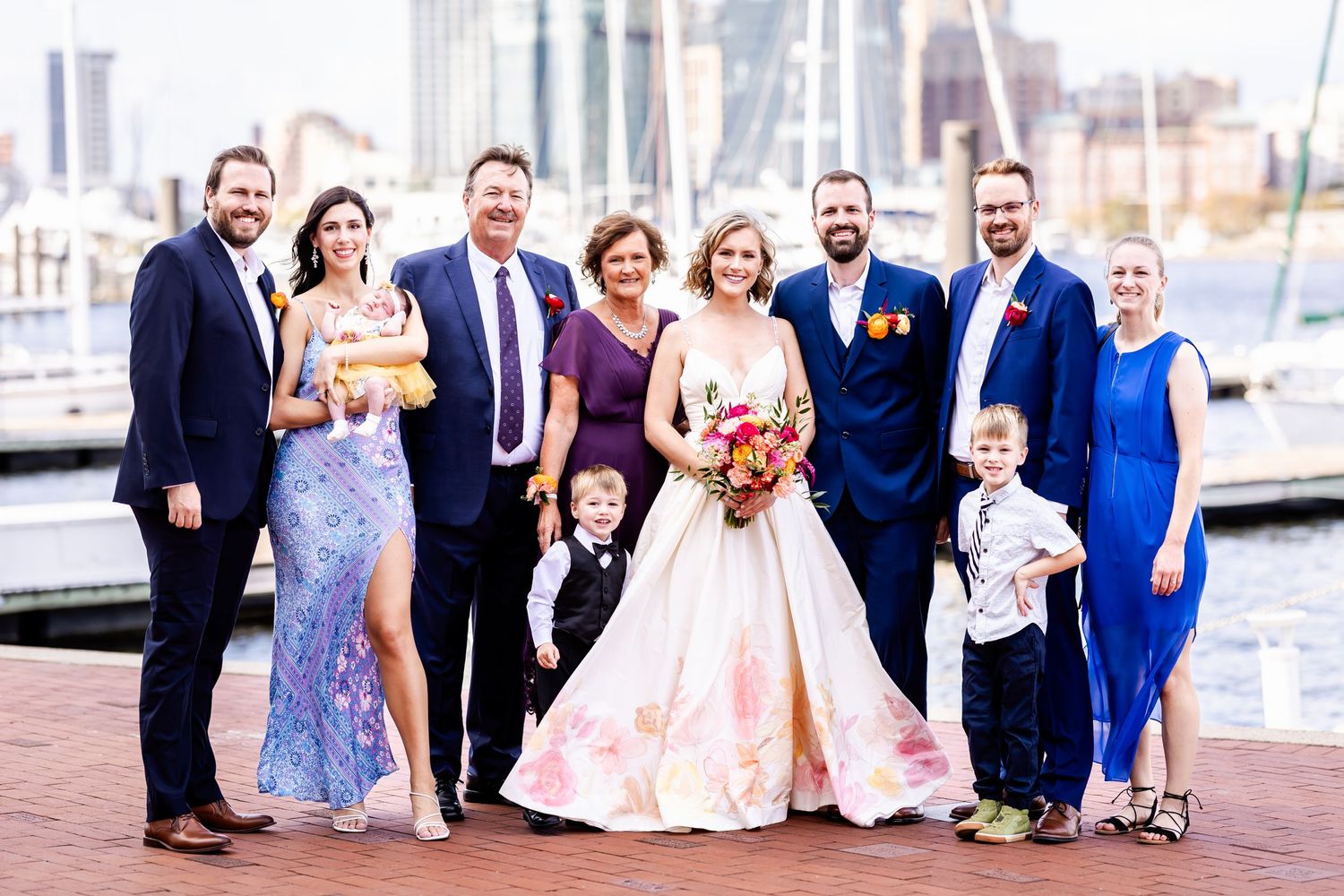 Wedding party poses together on a dock with boats and city skyline in the background.
