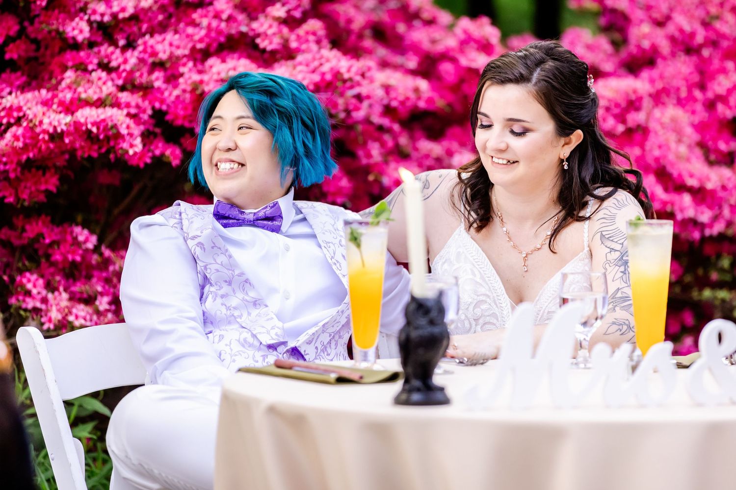 Wedding guests celebrate during toasts at outdoor tables decorated with bright pink flowering bushes.