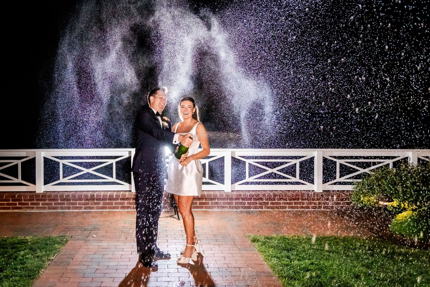 A romantic nighttime portrait of a couple in the rain with backlit water droplets creating a magical sparkle effect on a brick path.