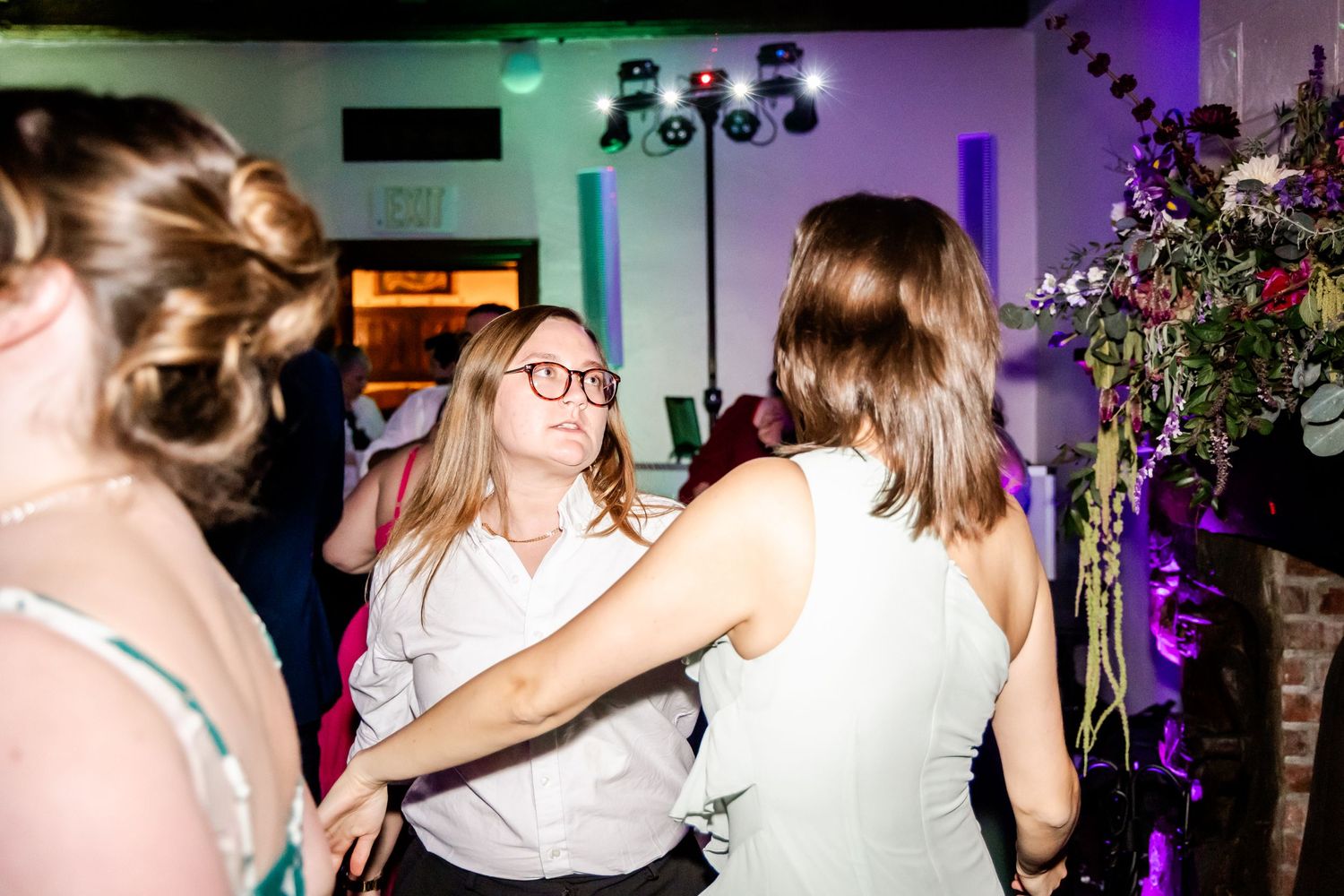Guests dancing and celebrating at a wedding reception with colorful lighting and floral decor.