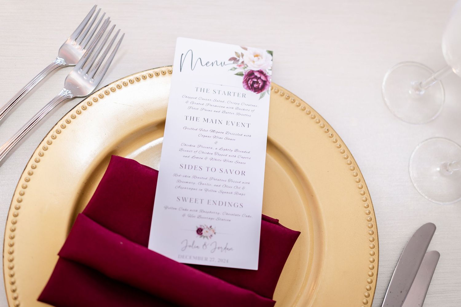 Place settings with burgundy napkins and menu cards on gold-rimmed plates.