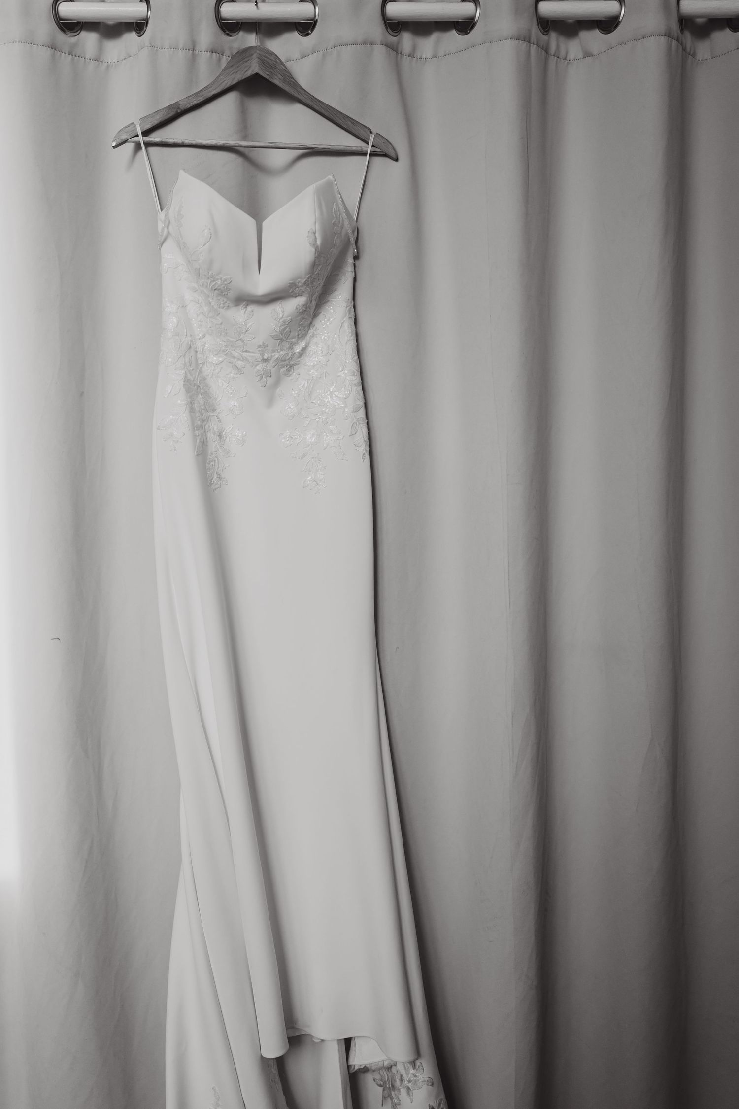 Elegant white wedding dress hangs on display against neutral gray background.