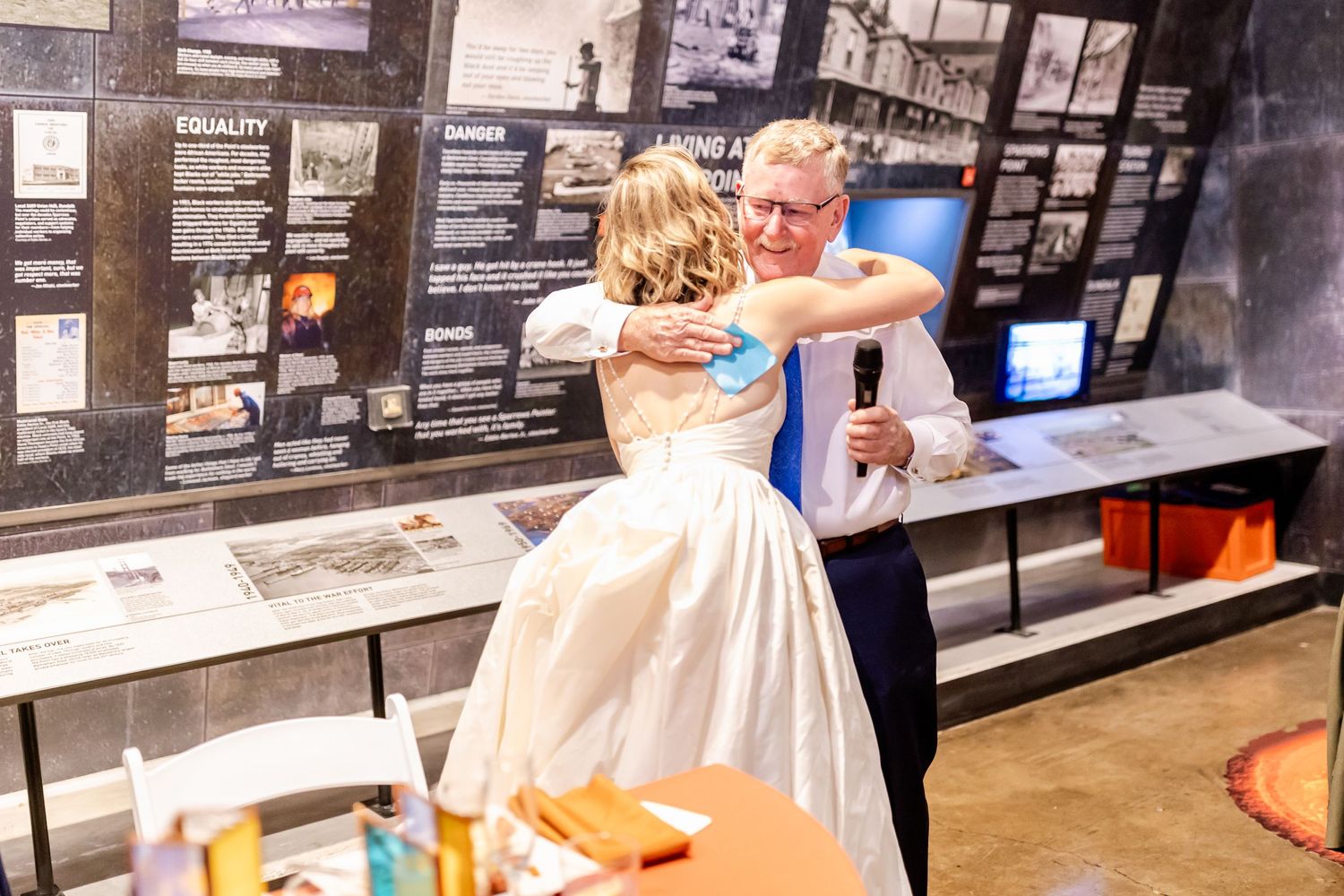 A couple dances together in formal wedding attire in front of a museum exhibition display.