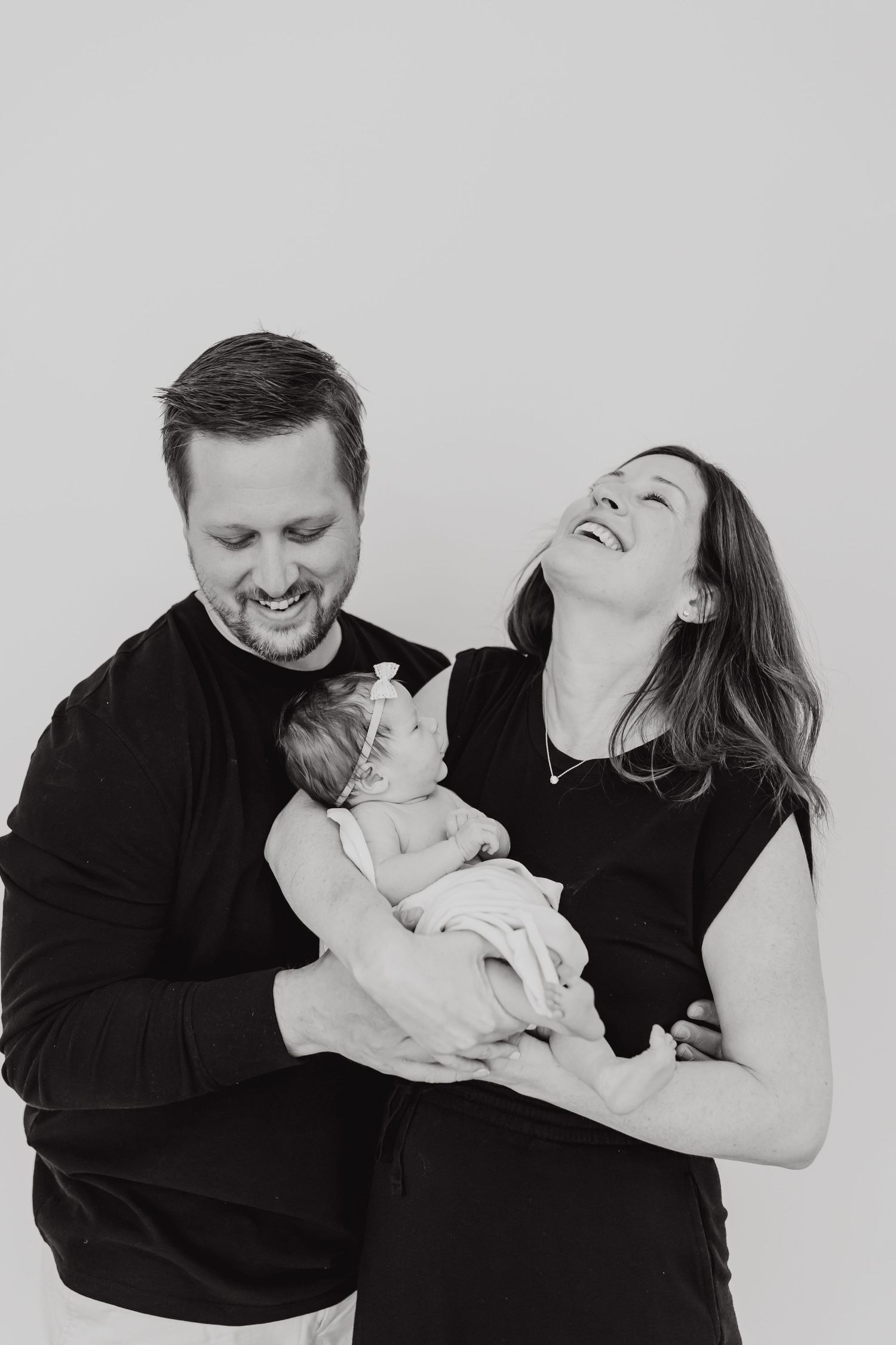 A candid family moment captured in black and white showing laughter and affection between parents and newborn.