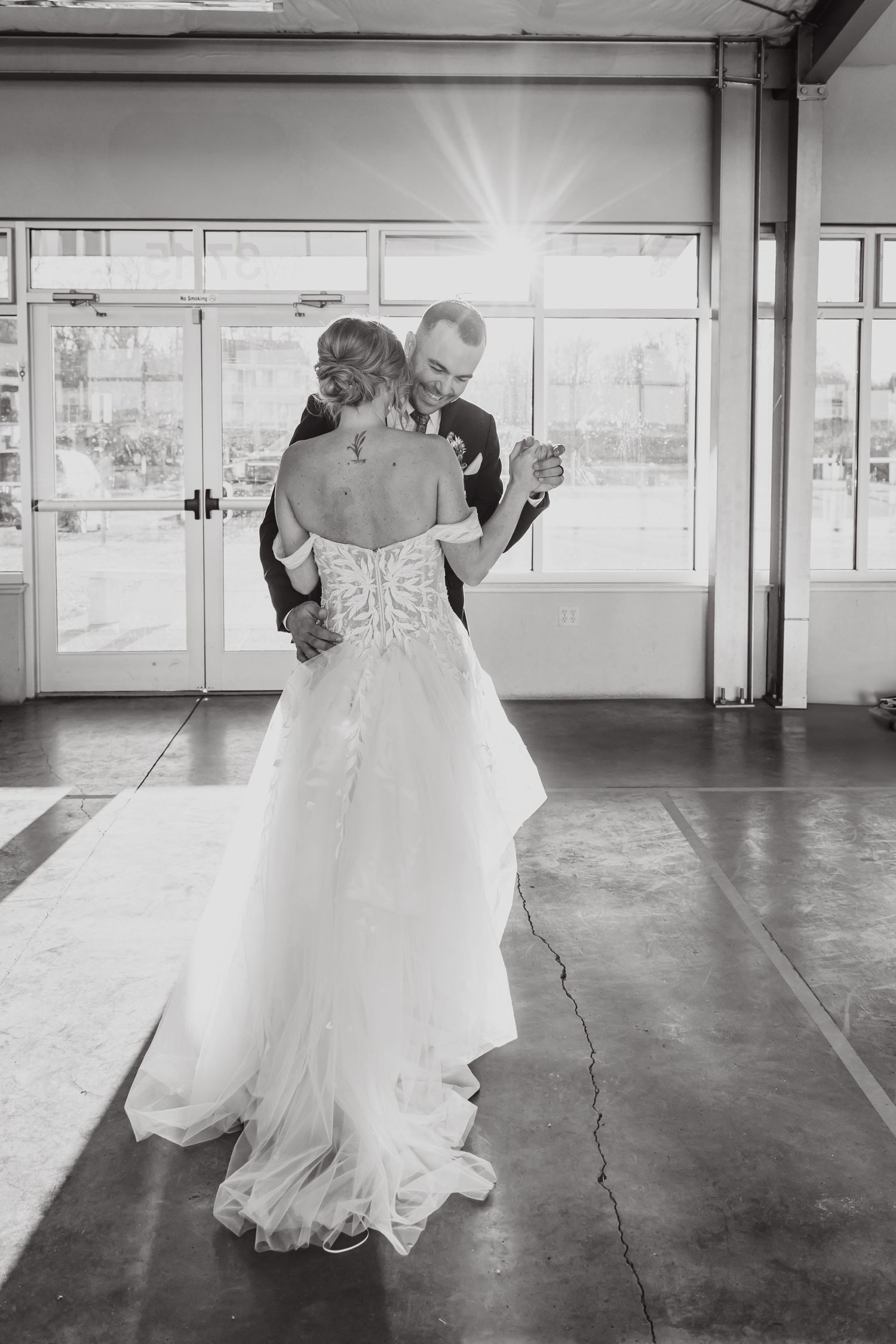A romantic first dance moment in black and white showing the back of a flowing wedding gown.
