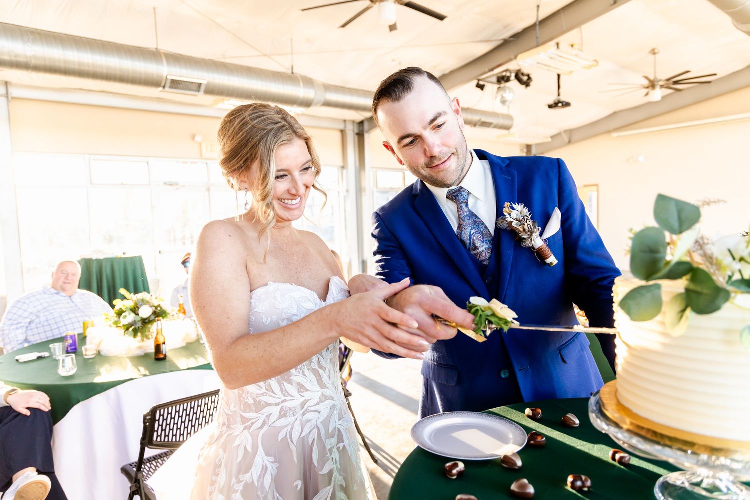 A couple in wedding attire cutting their elegant white wedding cake together at a reception.