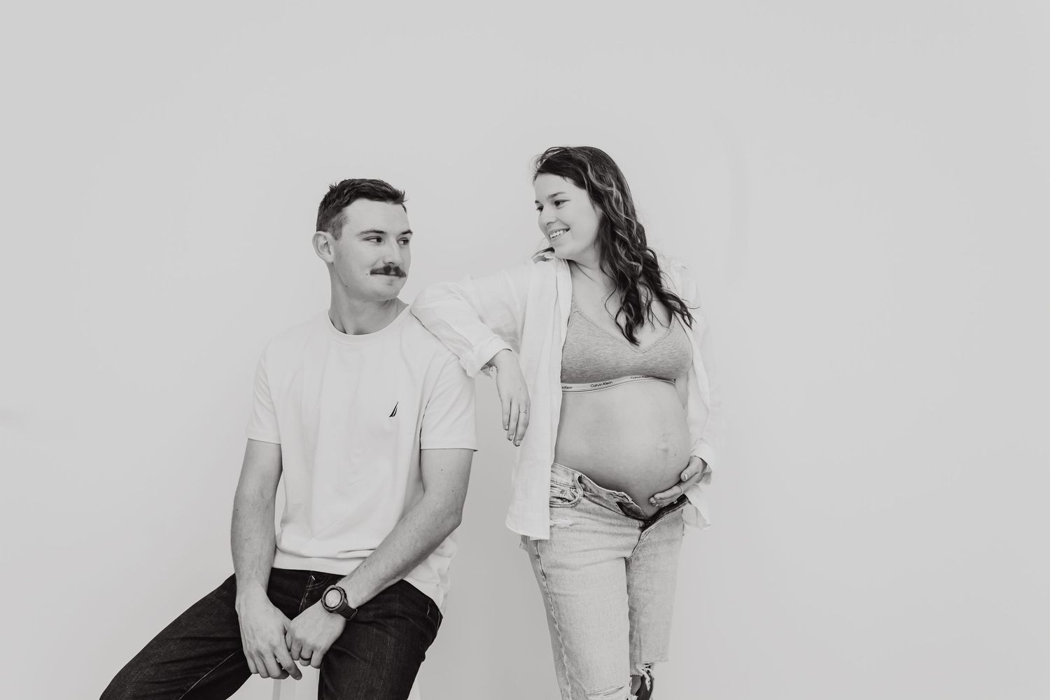 A black and white maternity photo shows an intimate moment between an expecting couple sitting together.