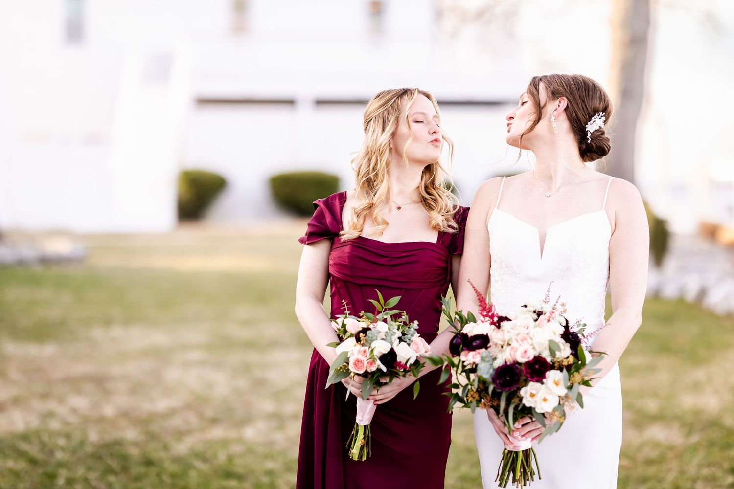 Wedding party members in burgundy and white dresses hold bouquets while walking and laughing together outdoors.